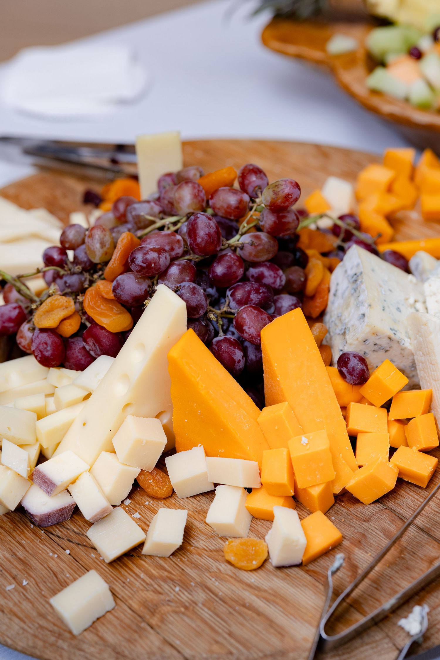 A rustic wooden charcuterie board displays cubes of cheddar and white cheese alongside fresh purple grapes.