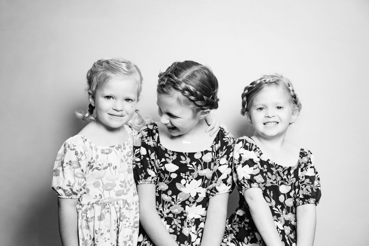 Three children in floral dresses pose together in black and white portrait photography.