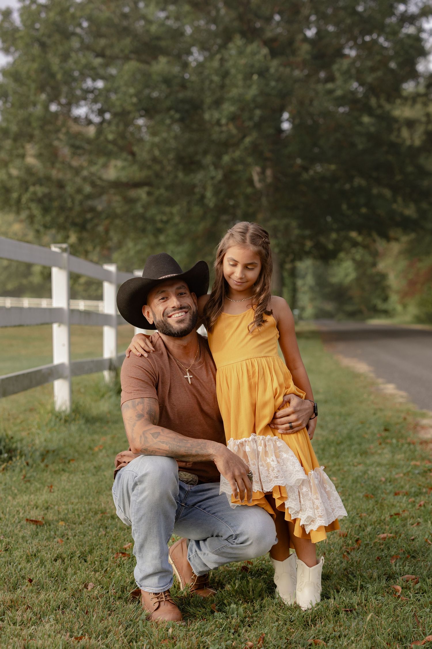 A parent and child share a tender moment outdoors on grassy ground near a white fence.