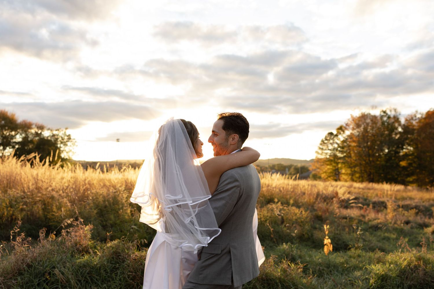 A couple shares a romantic moment in a golden field at sunset during their wedding photoshoot.