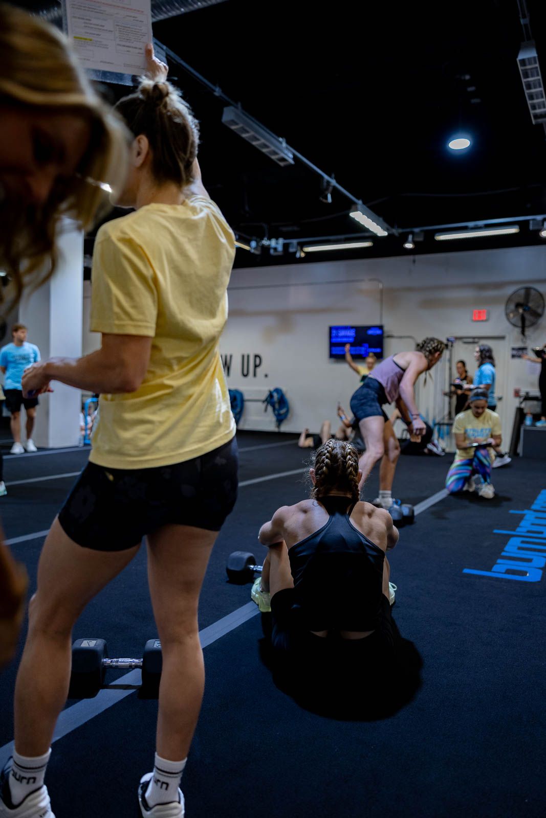 People exercising in a gym with yellow shirts and black shorts performing synchronized movements.