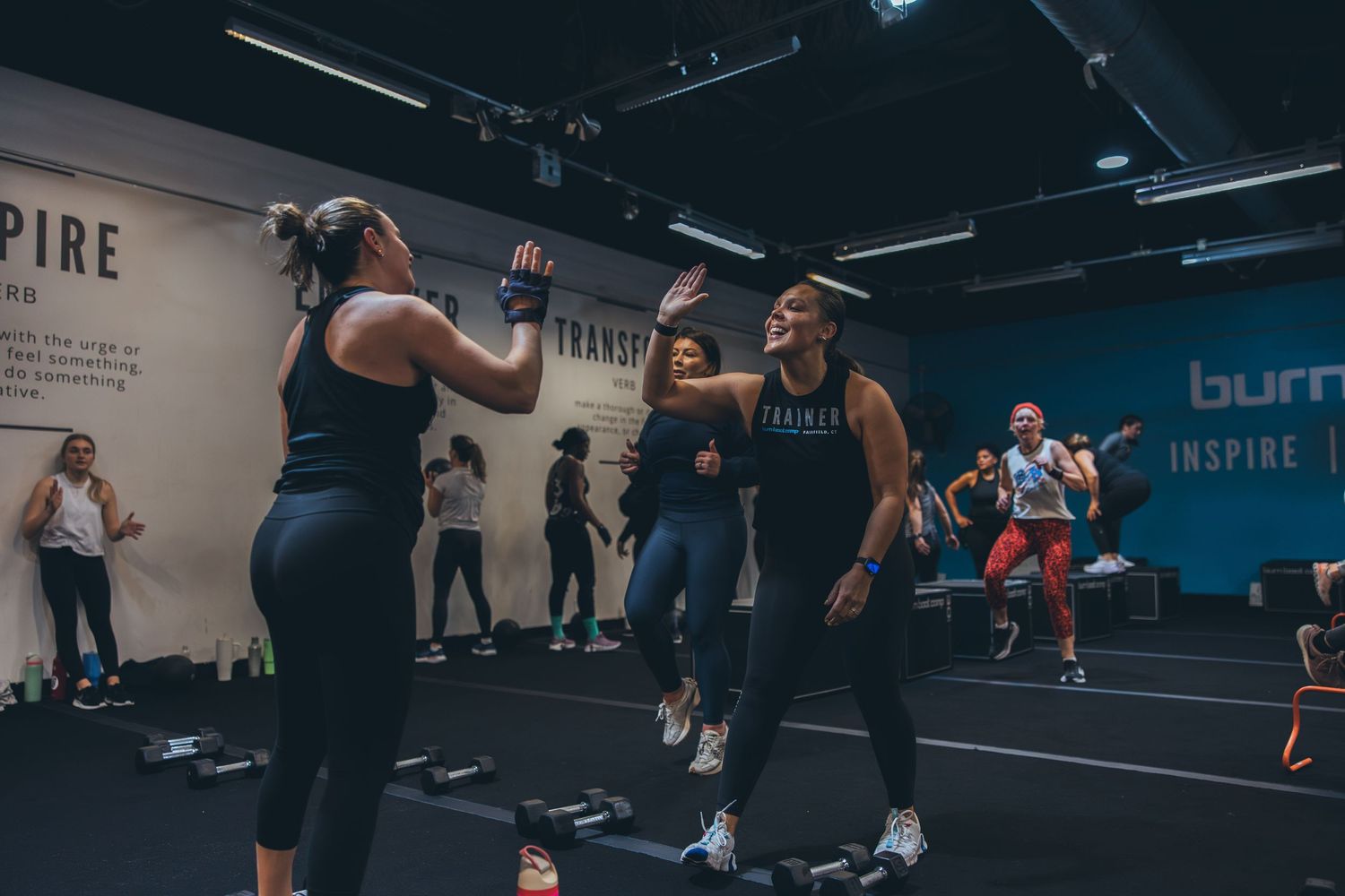 Group fitness participants exercise together in a dark gym with blue accent lighting.