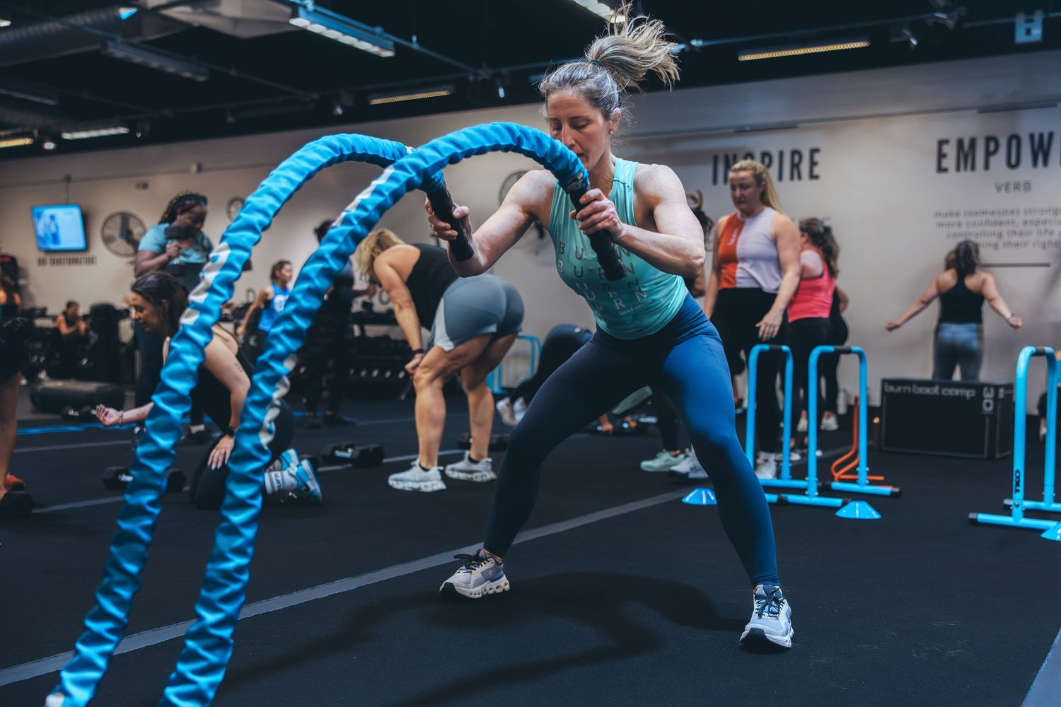 Participants swing blue battle ropes during an intense group workout session.