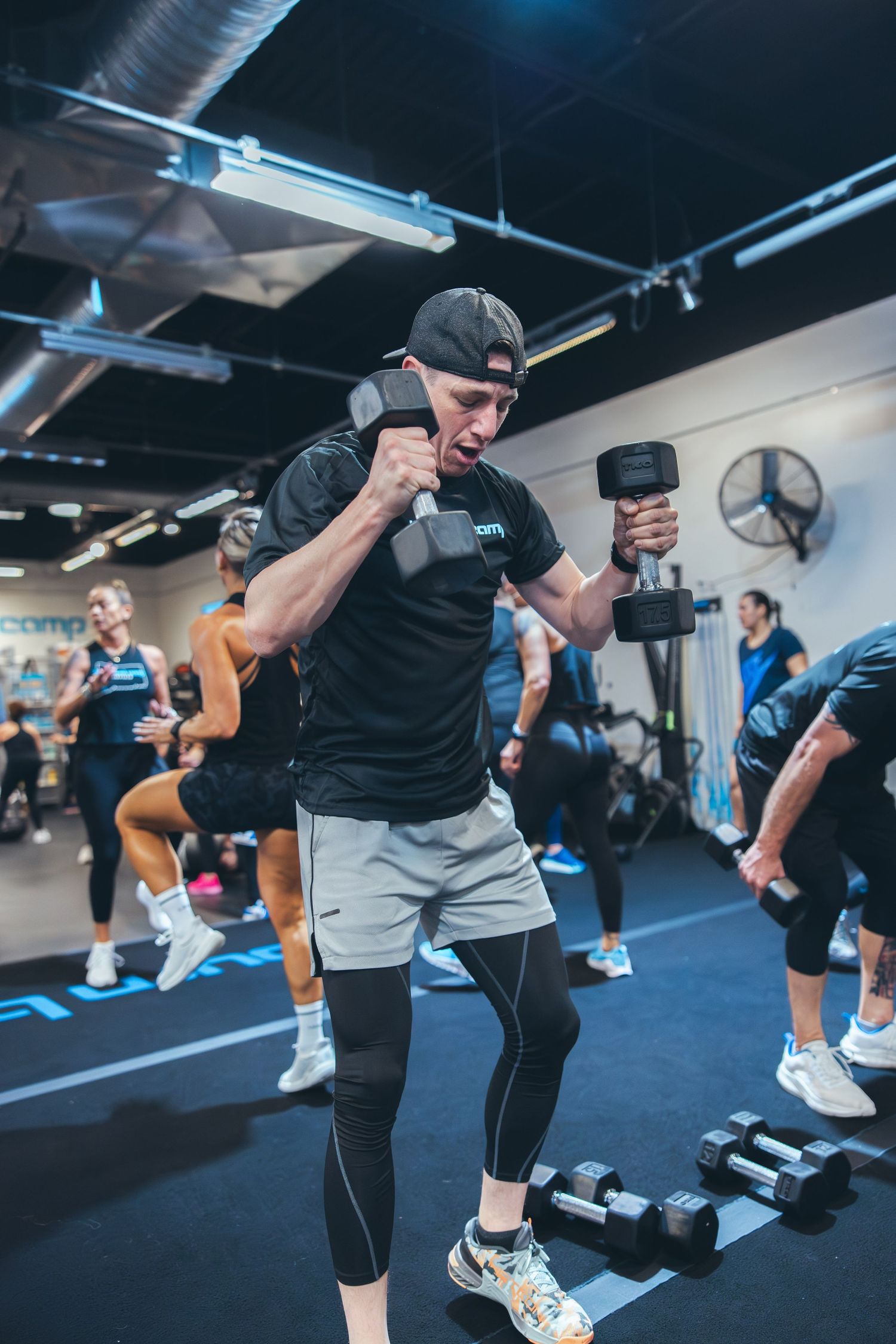 Athletic trainer demonstrating proper form with dumbbells during a gym workout session.