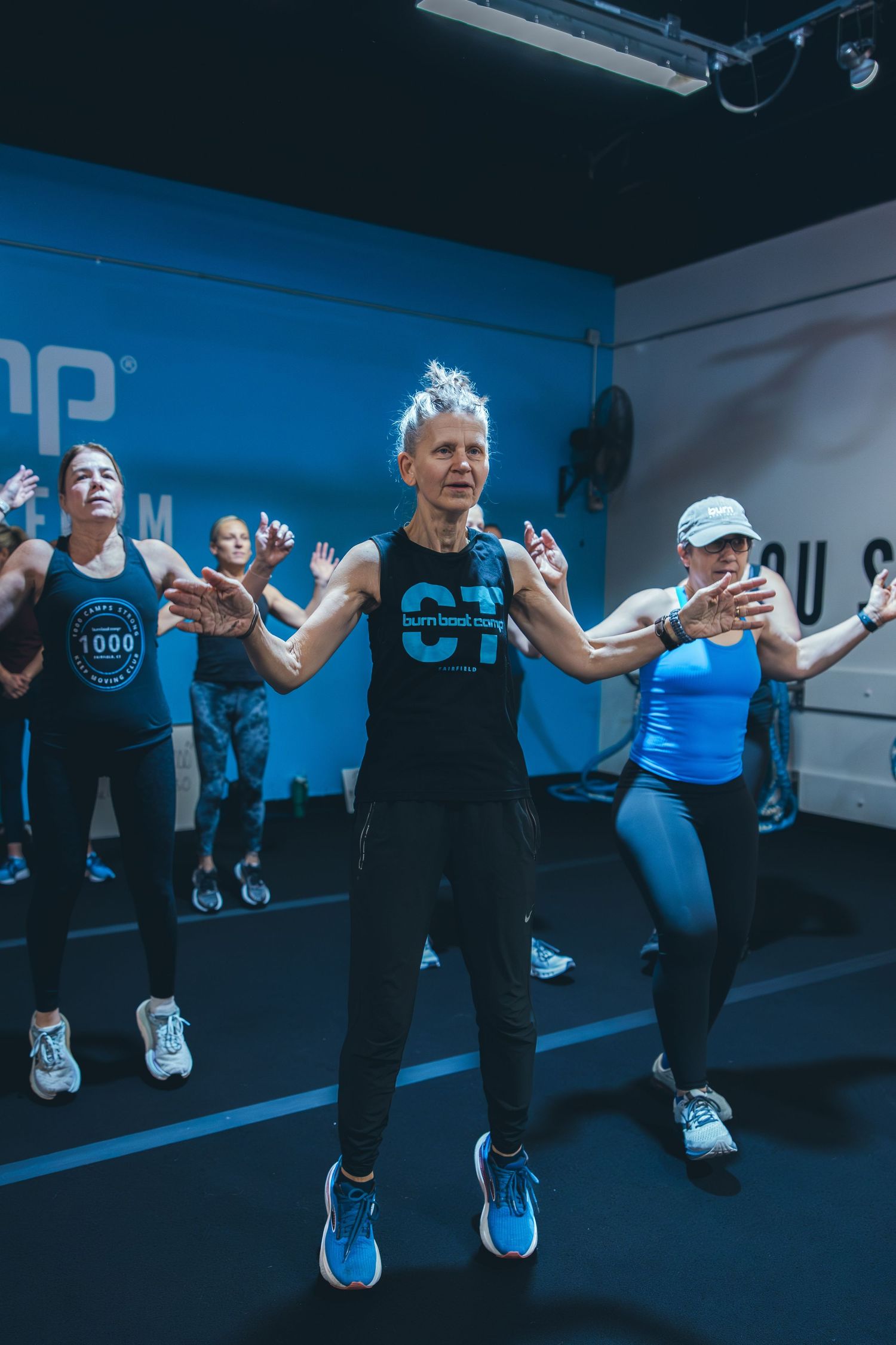 Group exercise class performing jumping movements in blue-lit fitness studio.