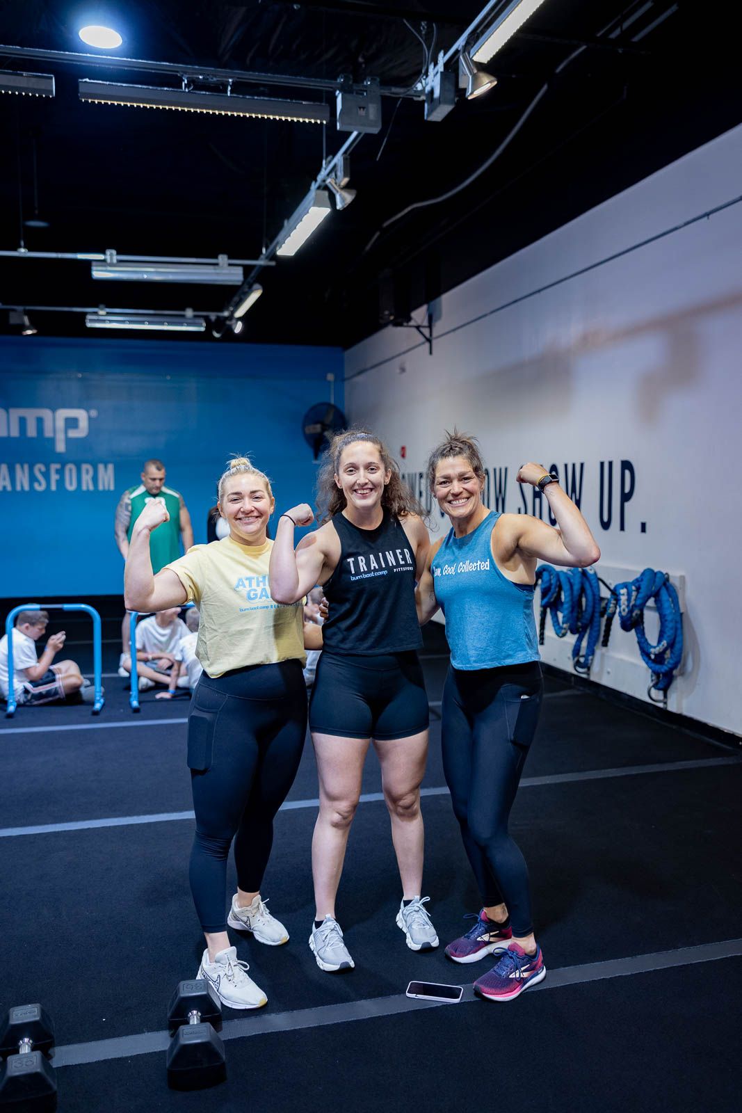 Group of athletes smiling and posing together at a CrossFit gym with blue walls during an evening workout session.