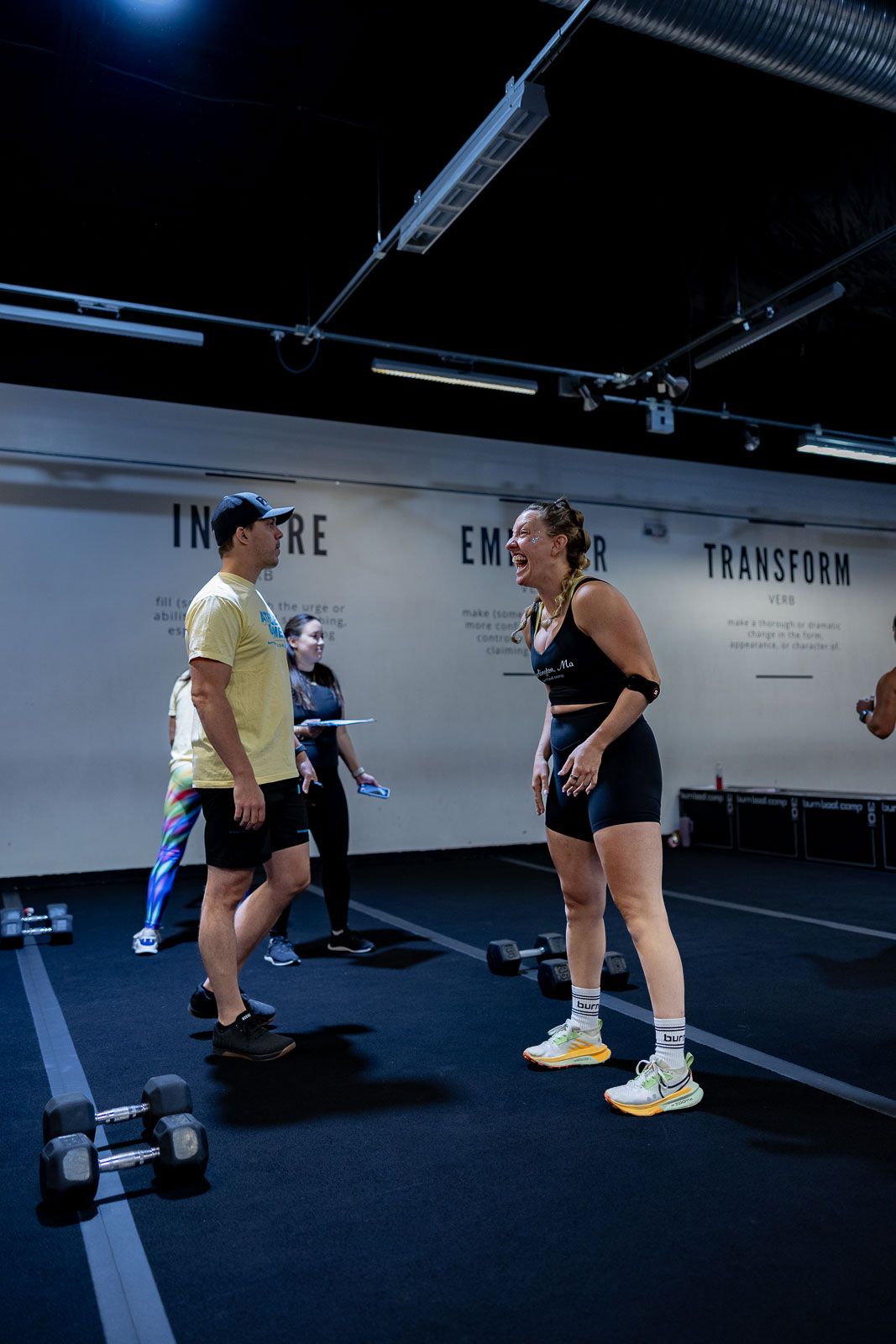 Athletes chat during a workout session in a modern fitness facility with motivational words on the wall.