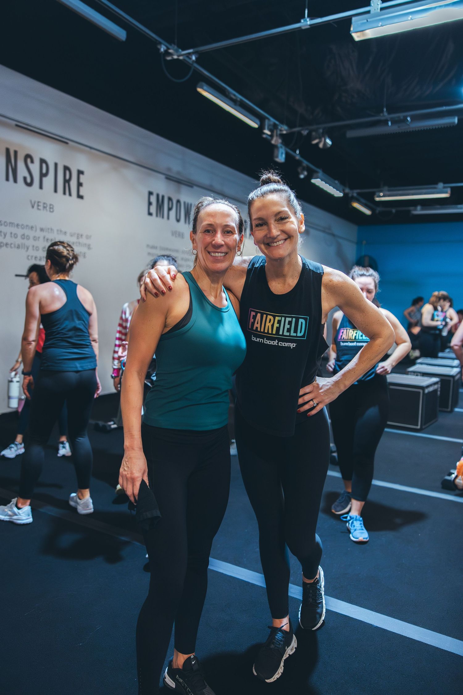 Workout partners sharing post-exercise moment at indoor fitness facility with inspirational wall text.