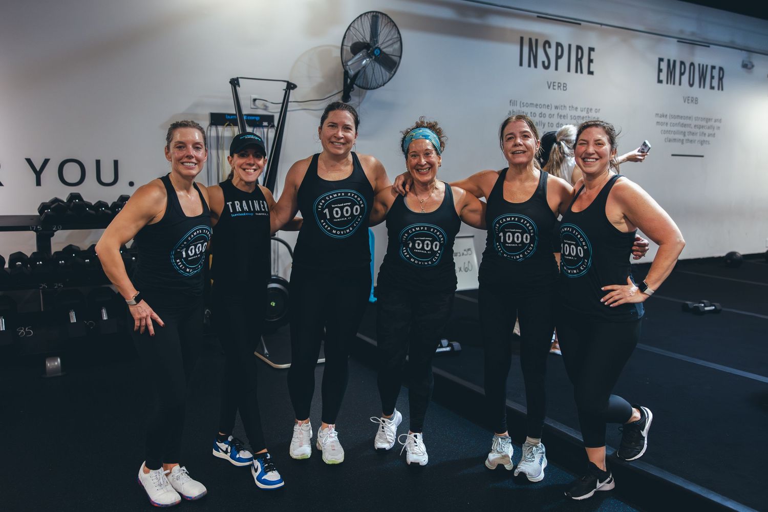 Team of fitness trainers in matching tank tops posing together at a modern gym facility.