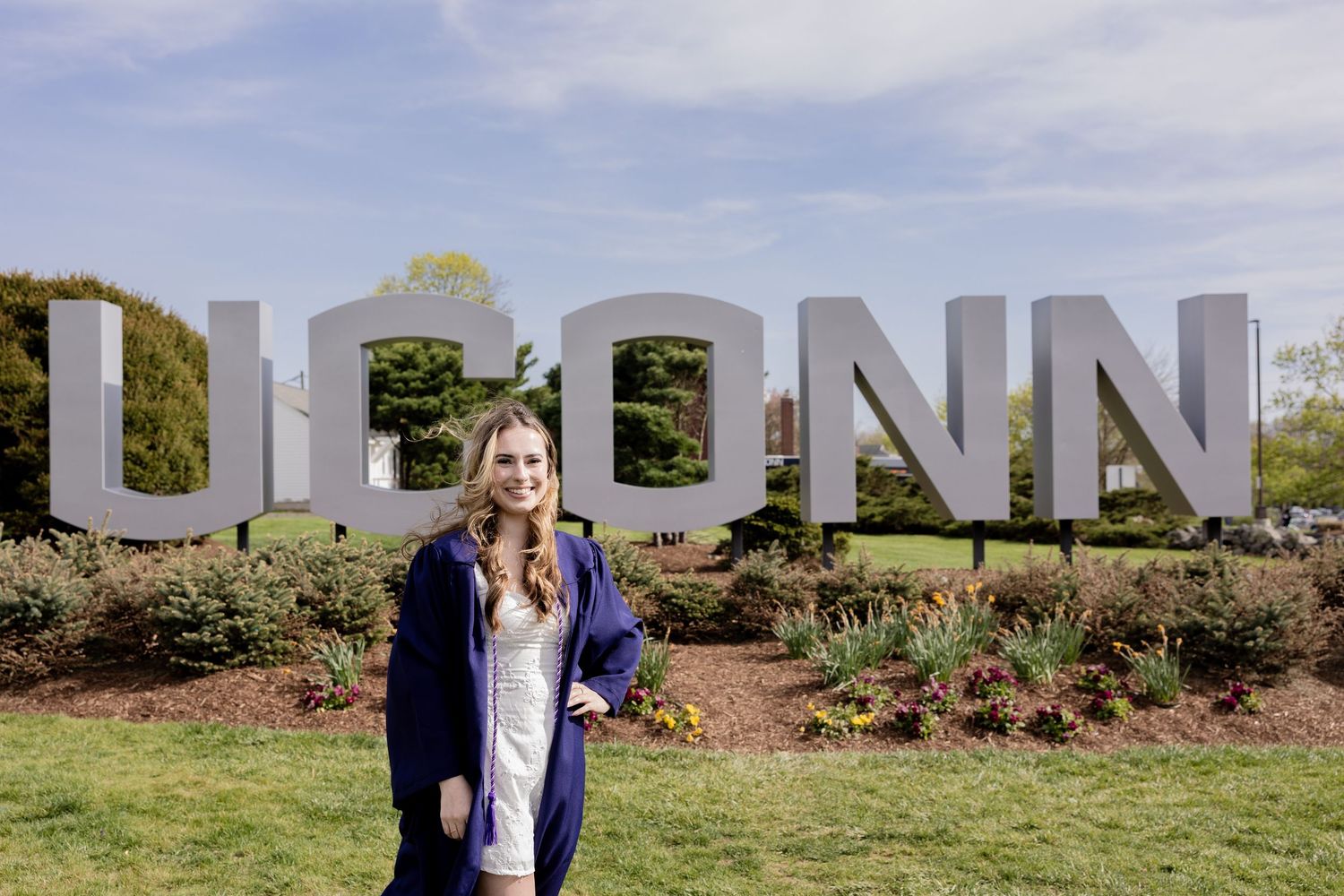 Large UCONN letters stand as an outdoor sign on a grassy lawn with landscaped garden beds.