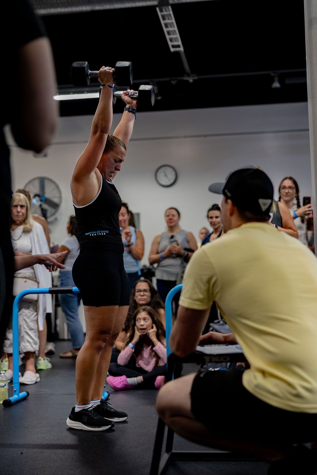 Indoor fitness class with participants working out beneath industrial-style ceiling with blue accents.