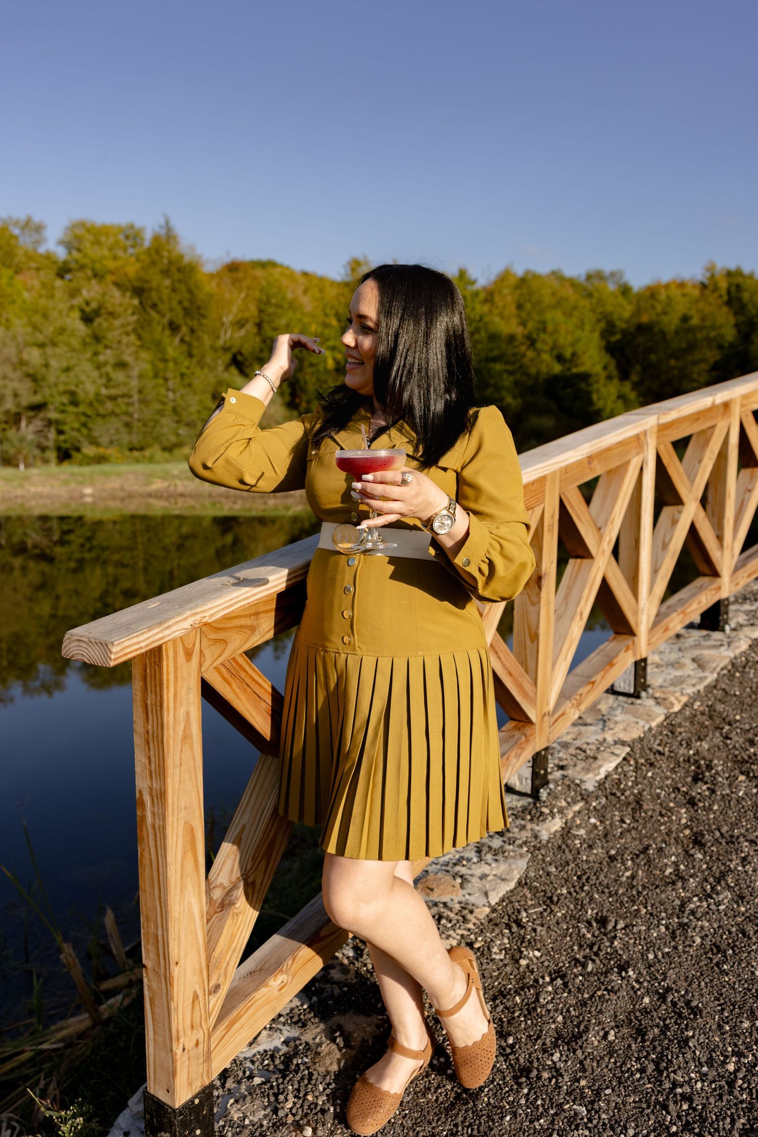 Person in a mustard yellow outfit posing on a wooden bridge overlooking a serene lake.