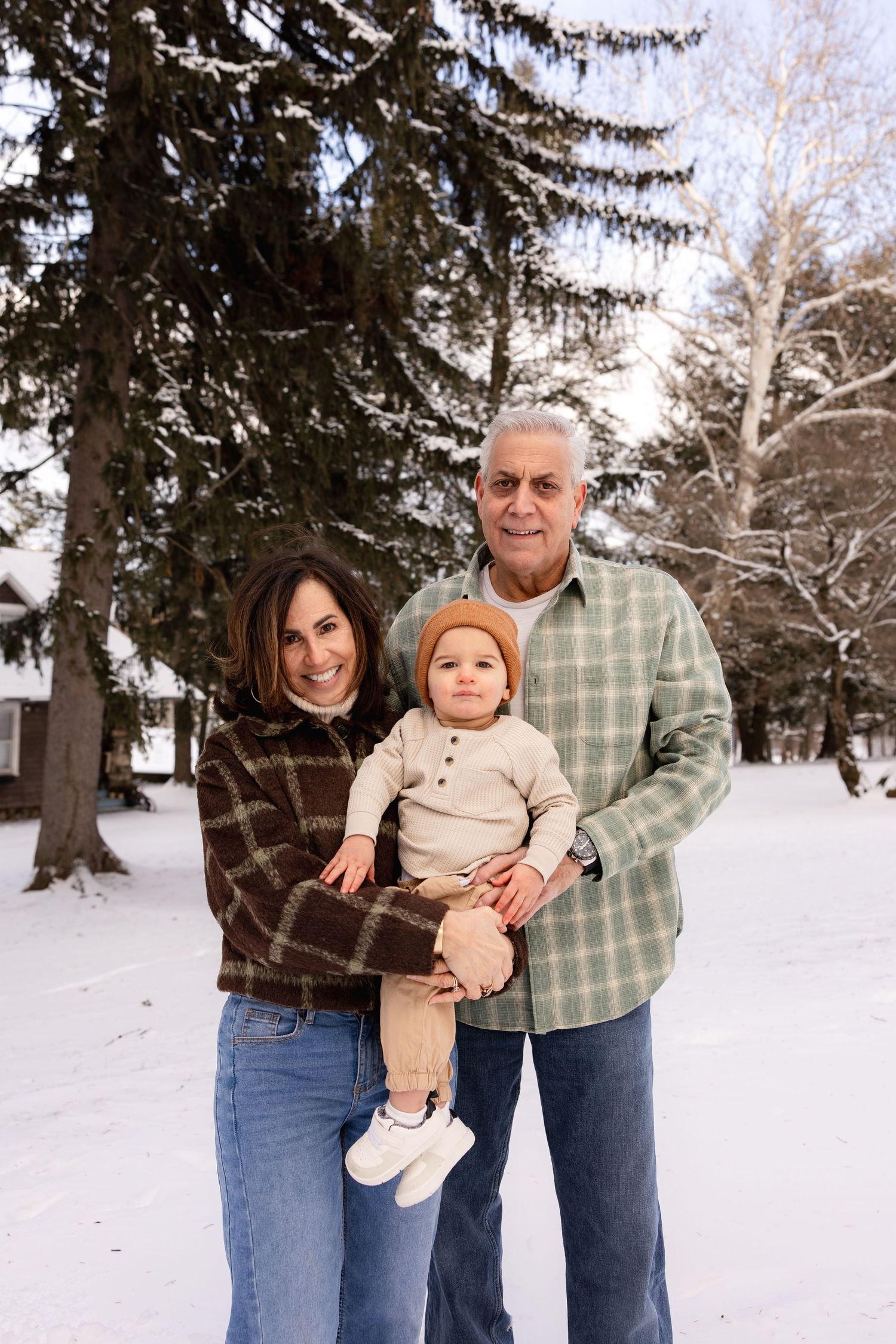 A family poses together in a snowy winter landscape with evergreen trees in the background.