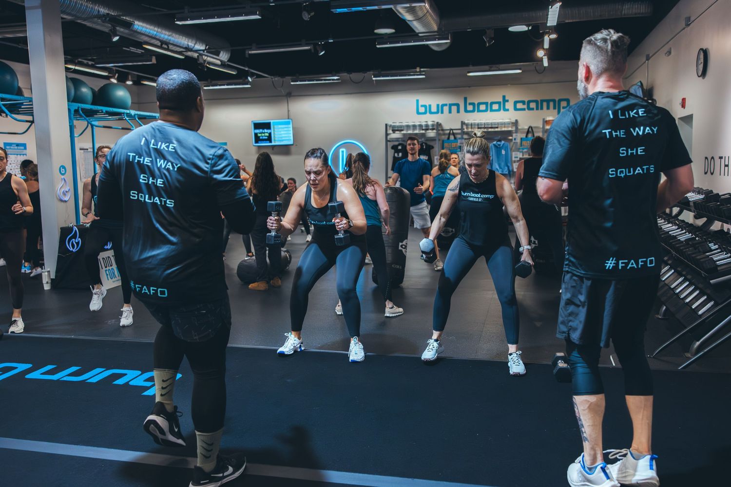 Group fitness class in progress with participants following instructors in a modern gym space.