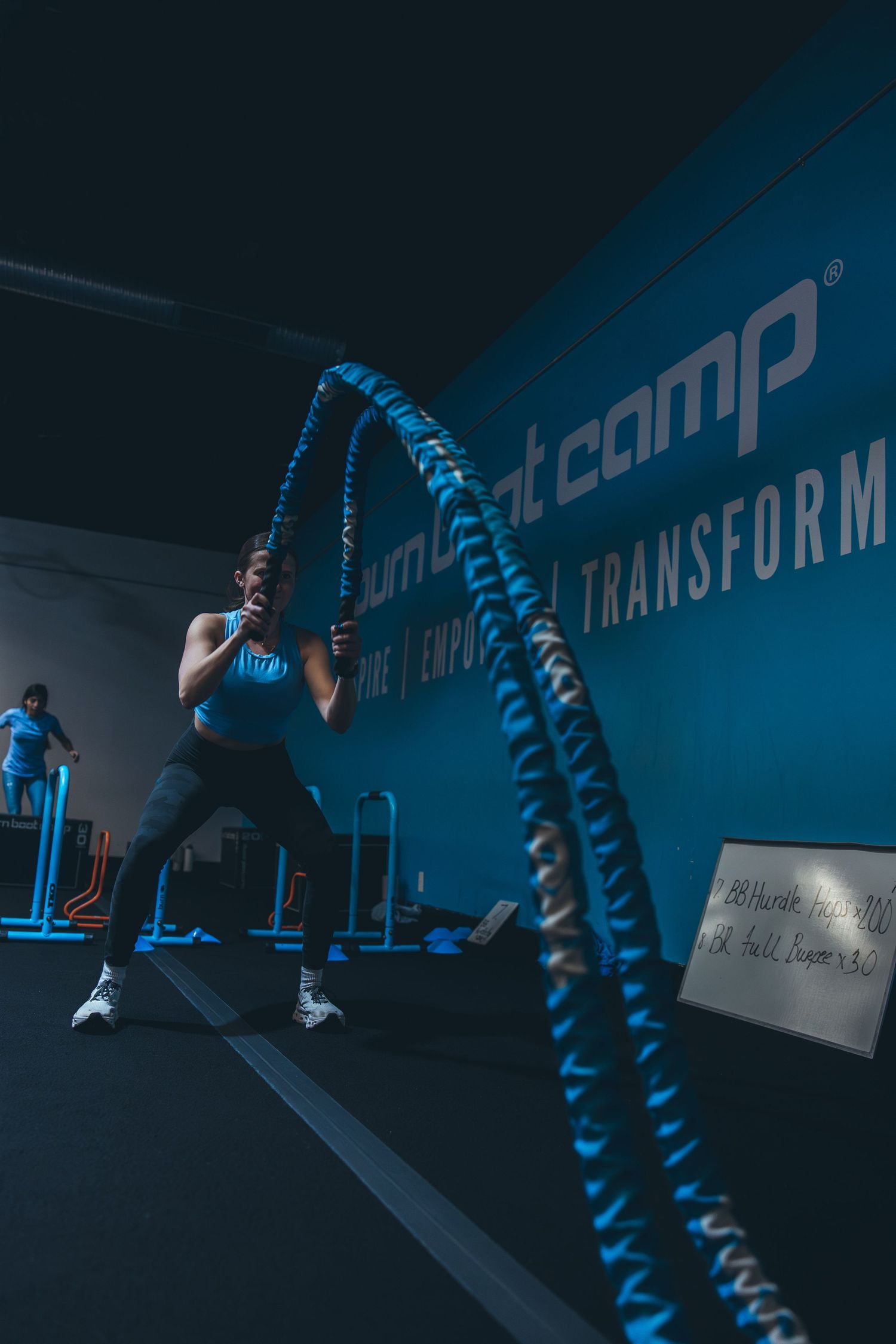Someone exercises with battle ropes in a dimly lit gym with blue accent lighting.