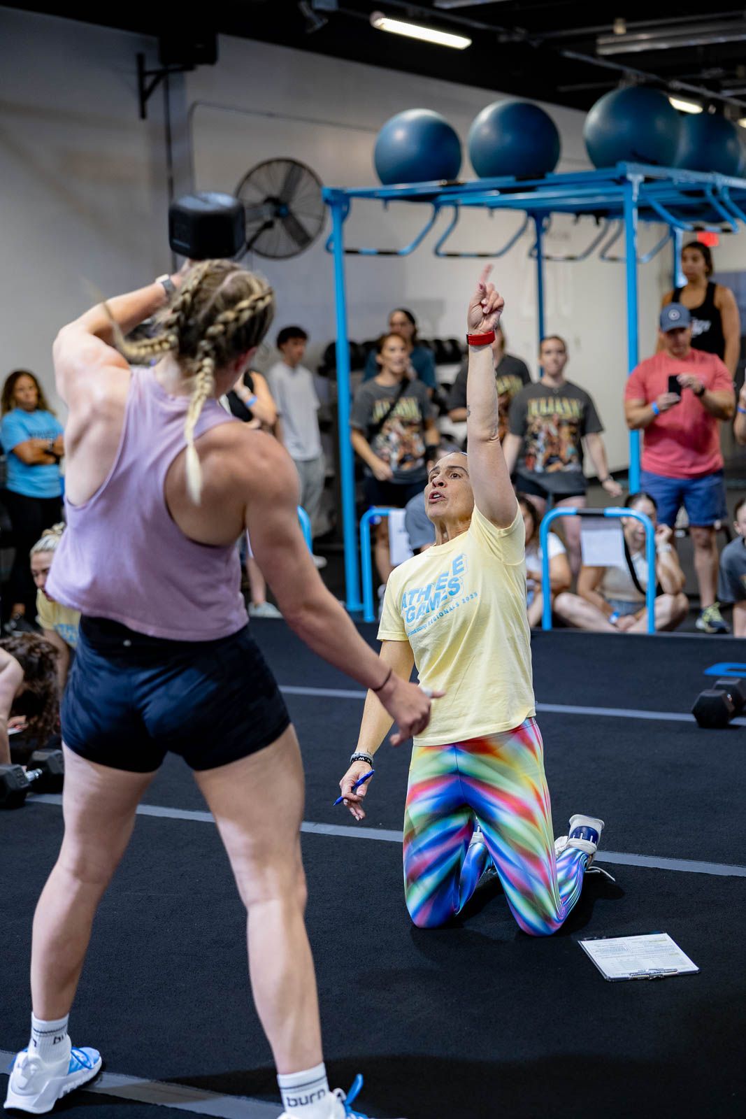 Athletes participating in an intense CrossFit workout session in a gym with blue equipment and spectators watching.