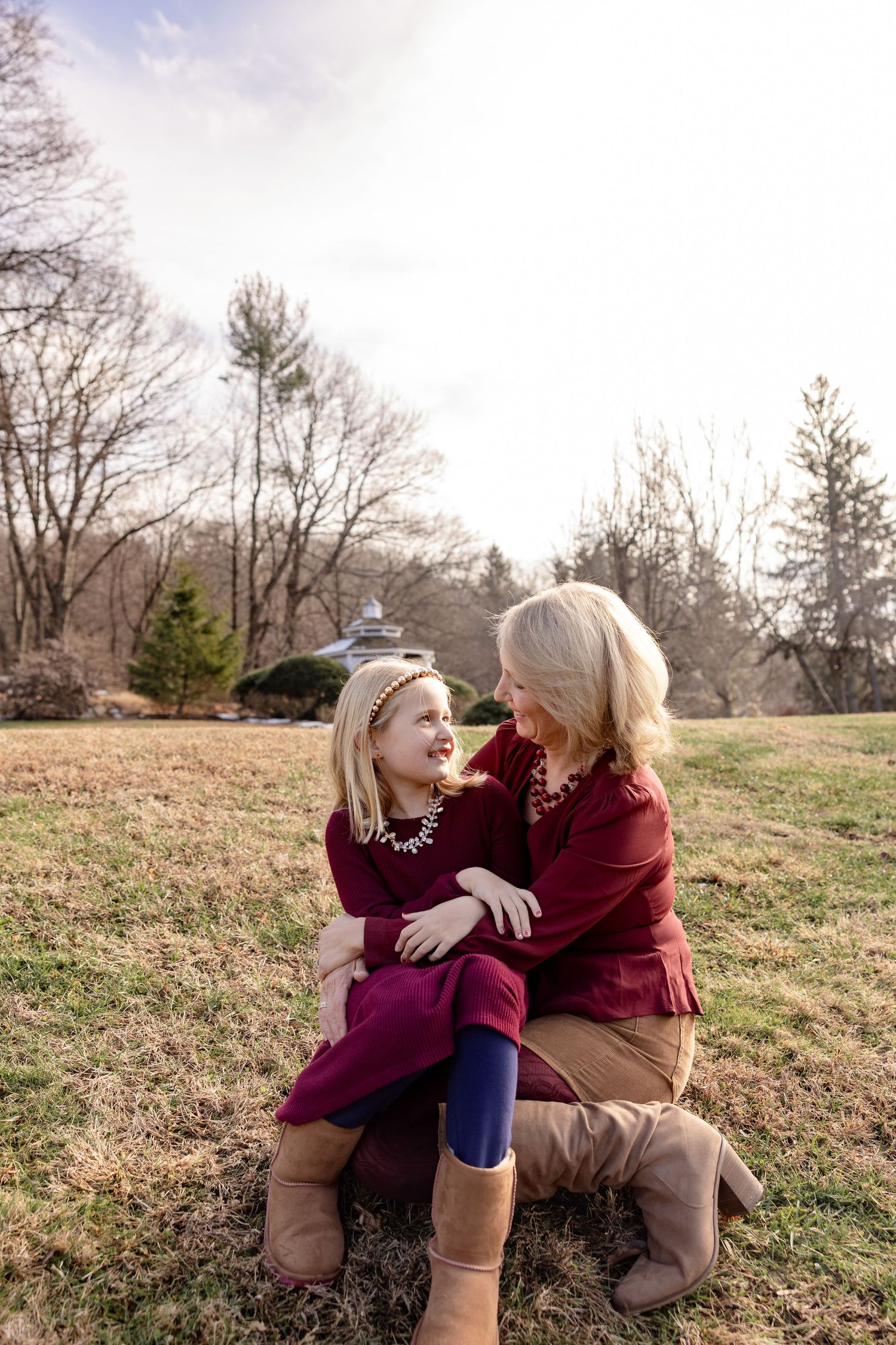 Two people in burgundy outfits share a joyful moment together while sitting in a grassy field on an autumn day.