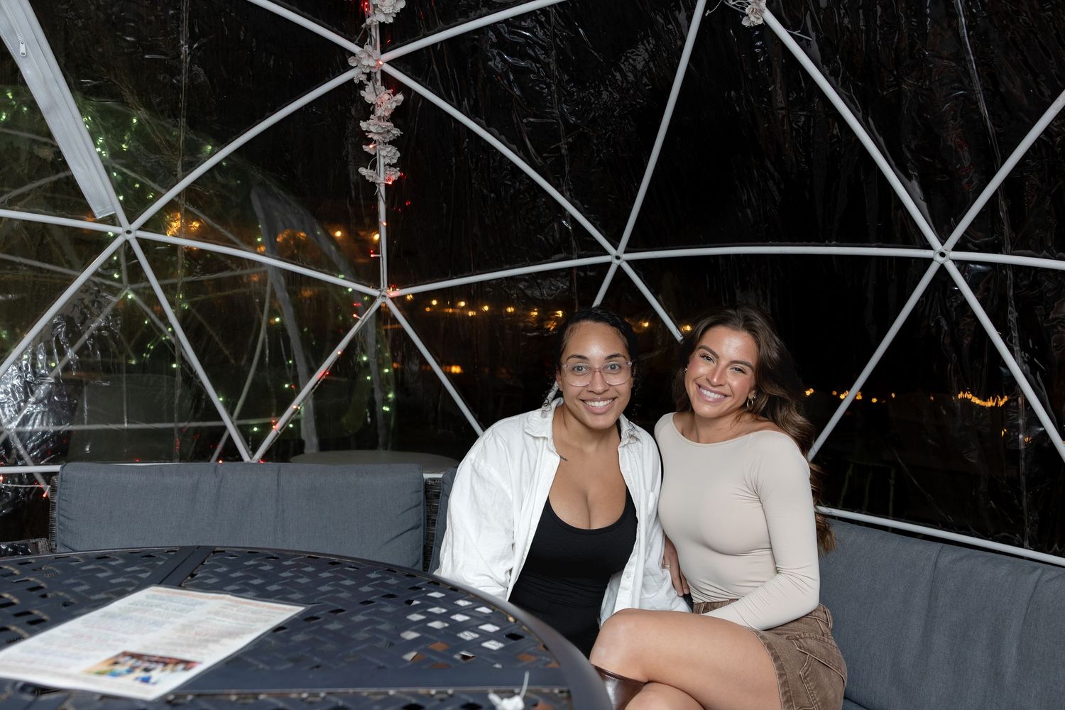 A group of people enjoying a nighttime gathering under a geodesic dome structure with string lights.