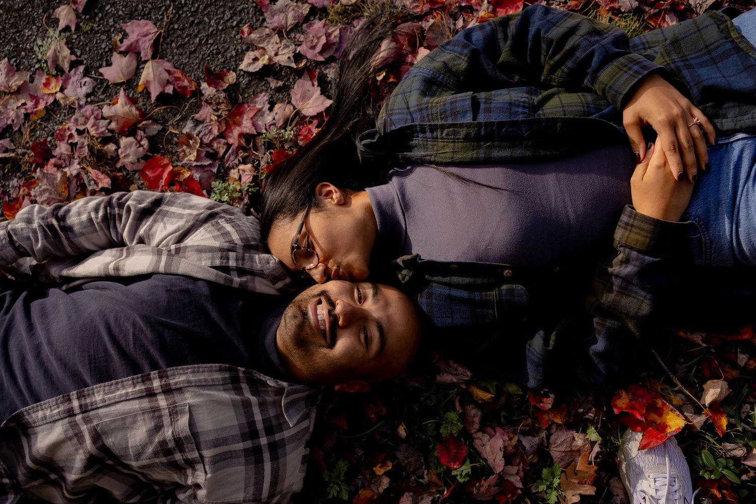 A person lies on the ground surrounded by scattered pink cherry blossom petals in a peaceful outdoor setting.