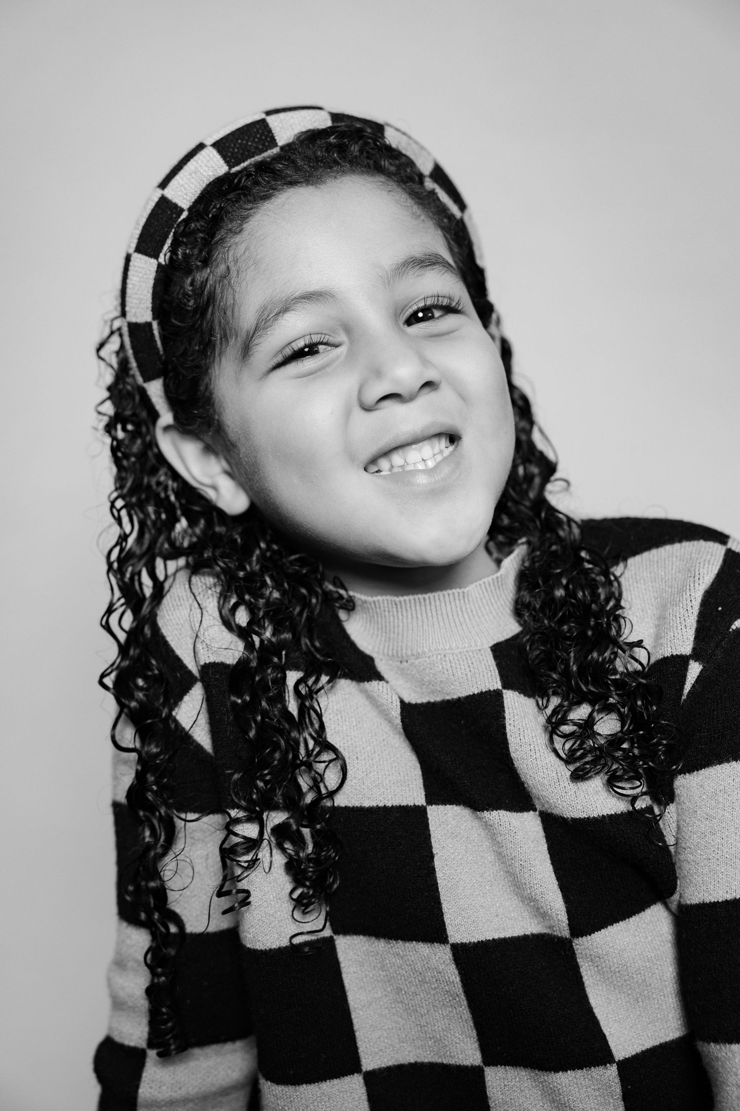 Black and white portrait of a child wearing a checkered pattern top and smiling warmly at the camera.