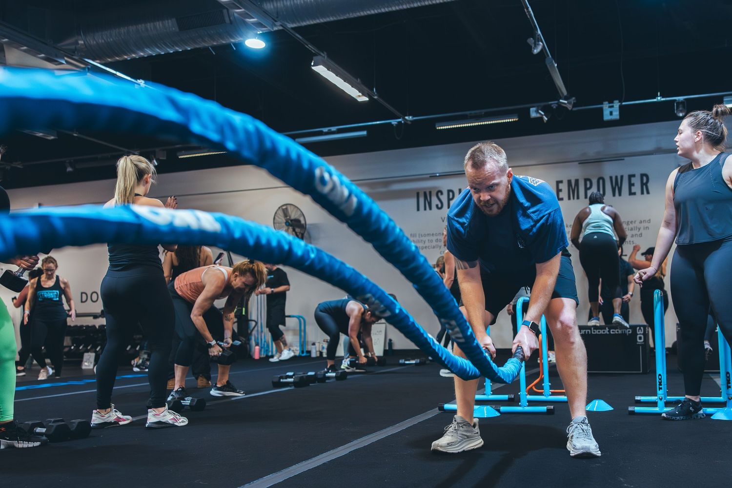 Exercisers train with blue battle ropes during an intense gym workout session.