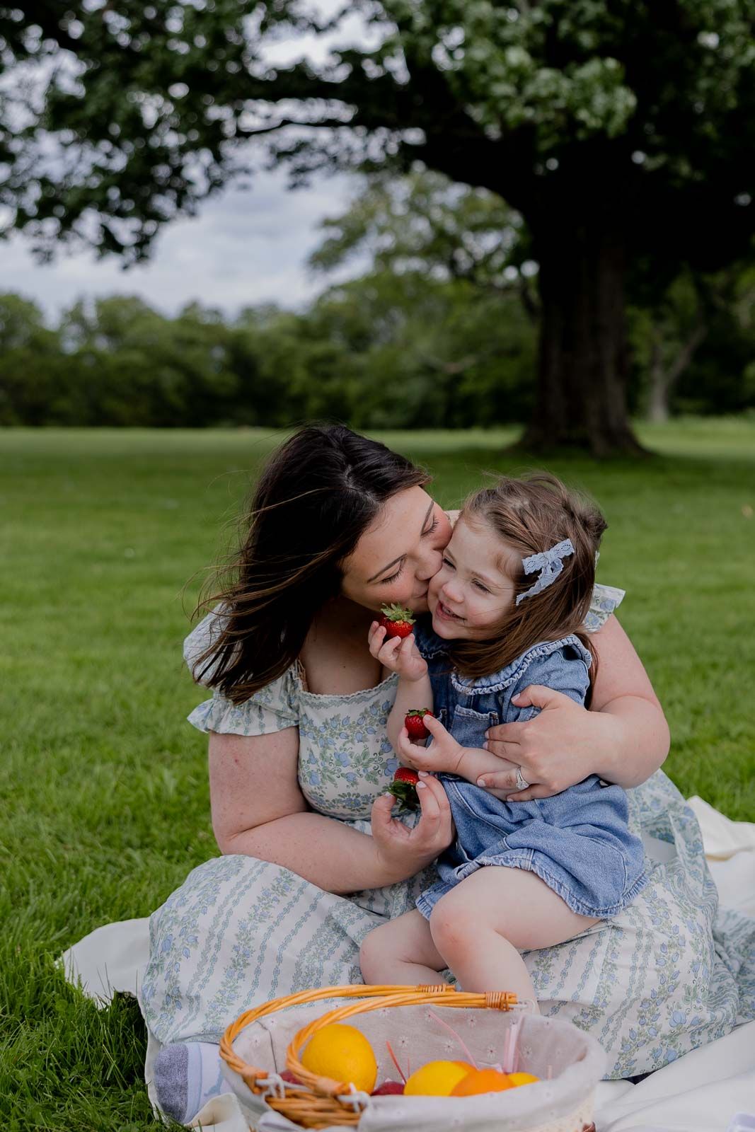 A tender moment shared during a picnic on a grassy lawn under a large tree.