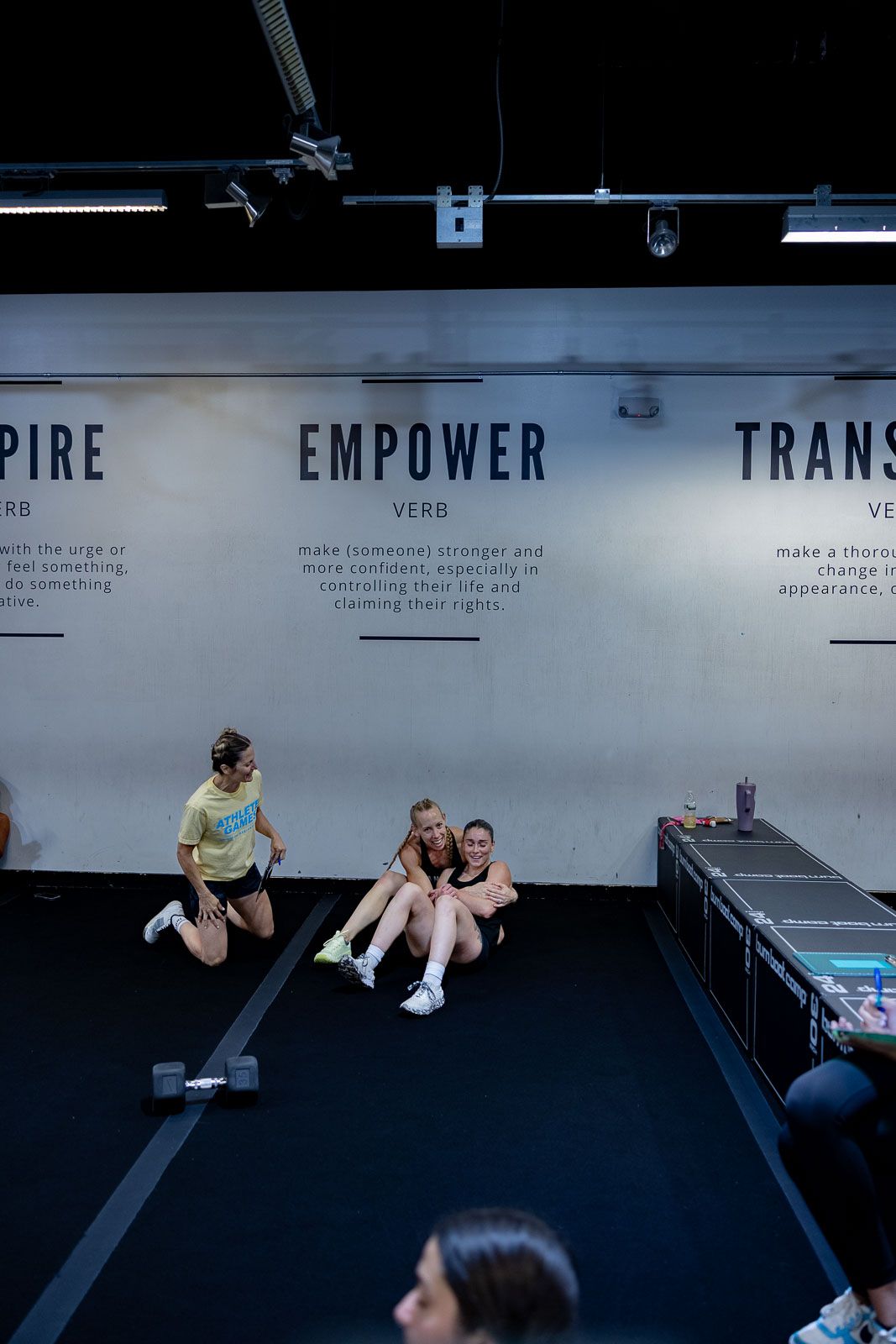Gym interior showing wall text with words 'Empower' and people resting on exercise equipment.