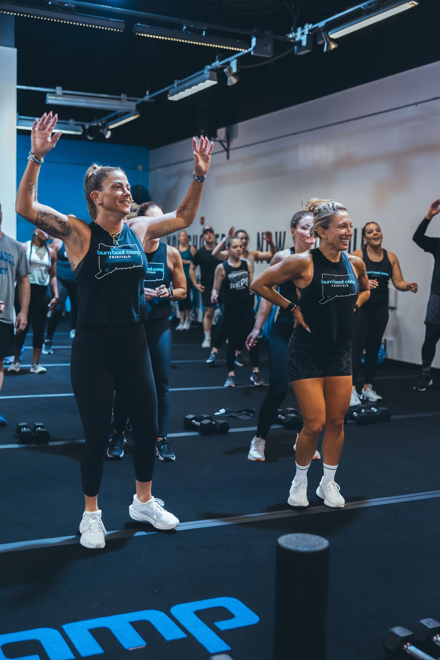 Energetic workout class participants with raised arms following instructor moves in a modern gym.