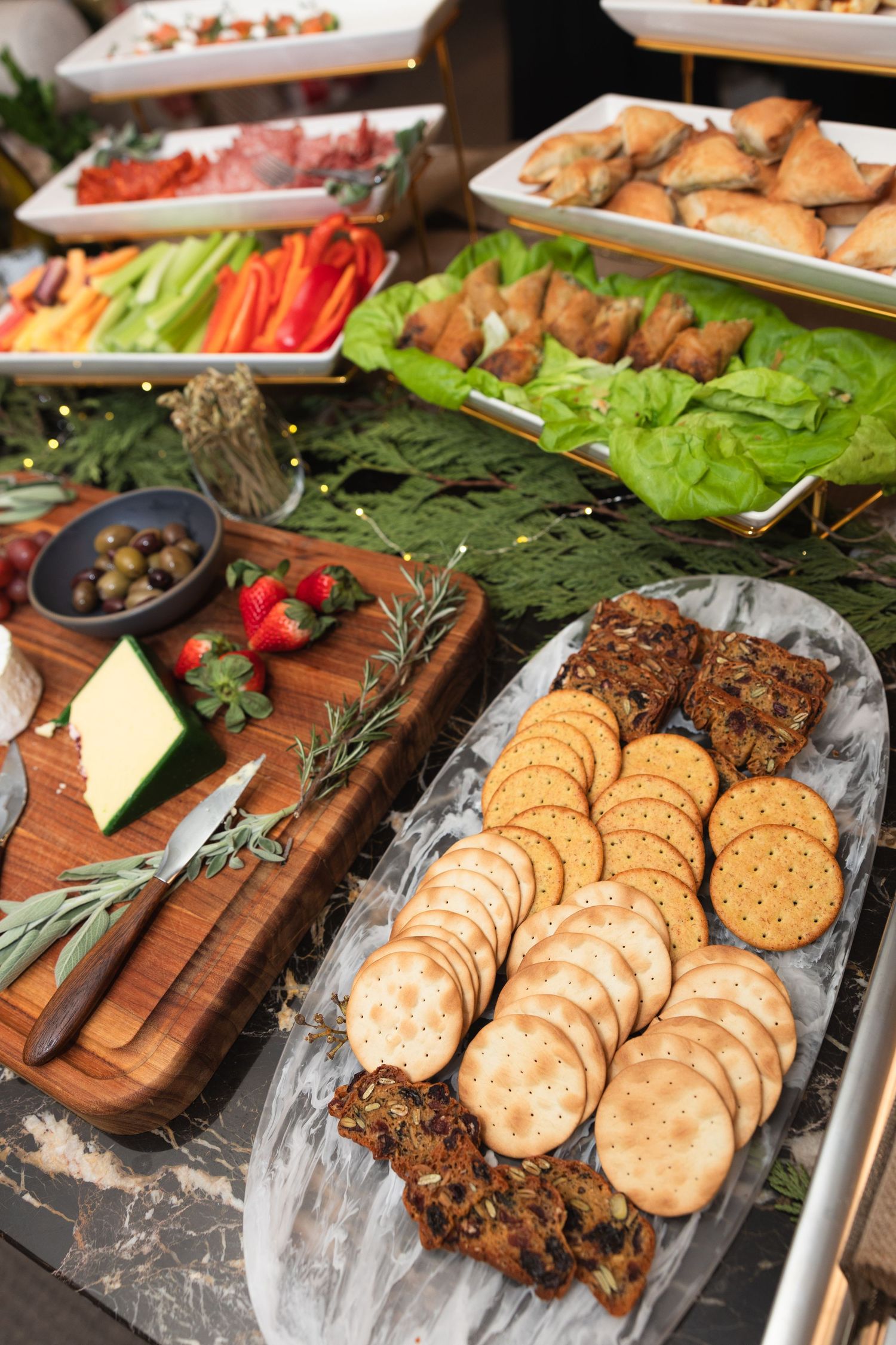 A charcuterie board with crackers, meats, cheeses, and fresh vegetables arranged on wooden serving platters.