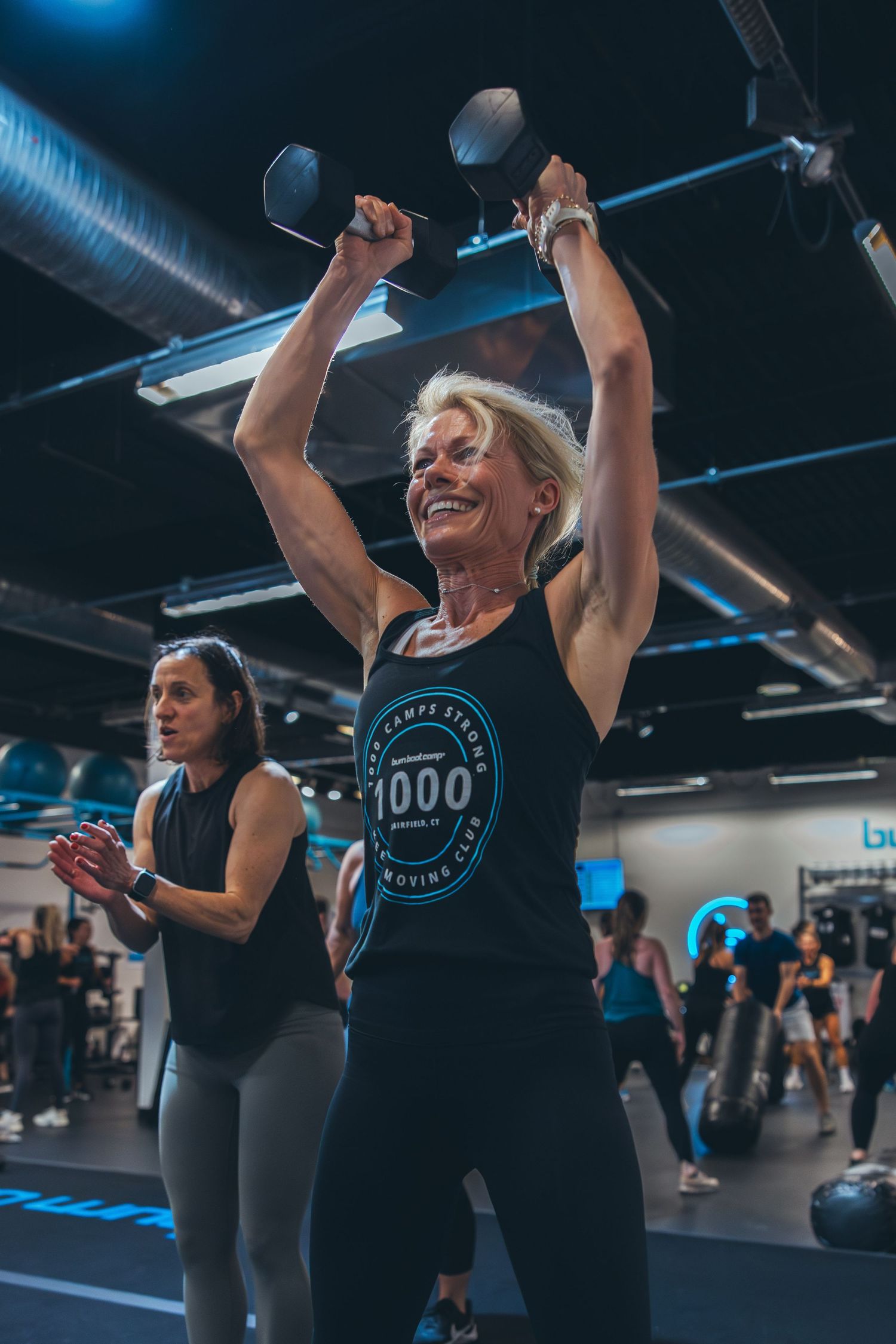Participants raise weights overhead during an energetic group fitness class in a modern gym facility.