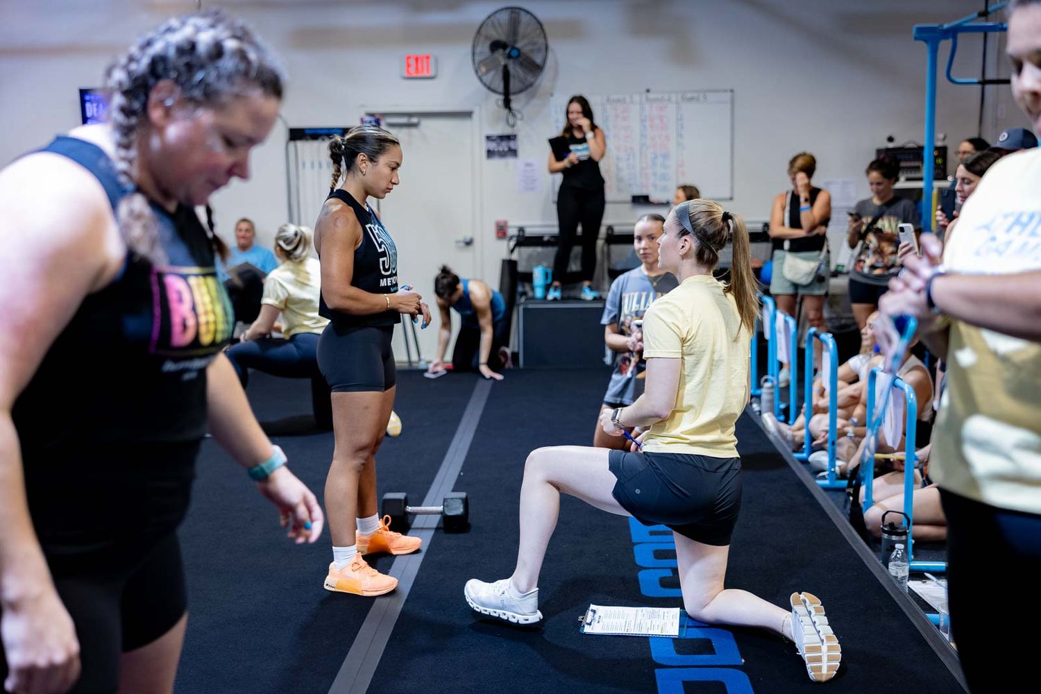 Group fitness class participants exercising together in an indoor gym space with blue lighting elements.
