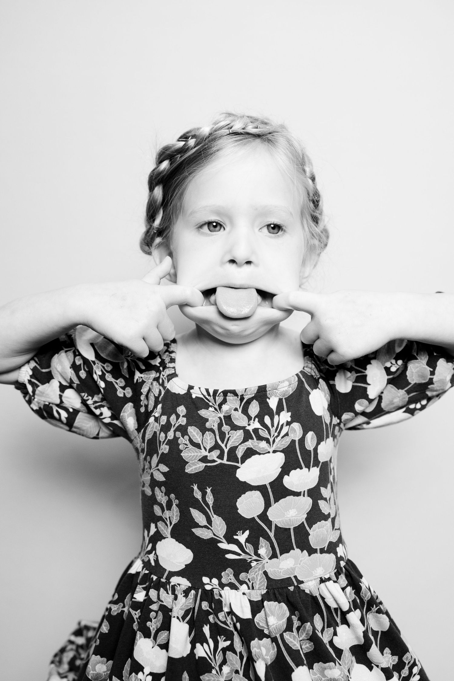 A playful sequence of black and white photos showing a child in a floral dress making silly faces and poses.