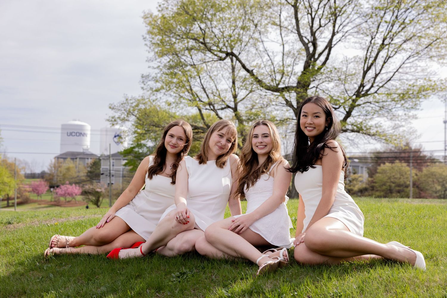A group of friends in white outfits relaxing together on grass in a park setting.