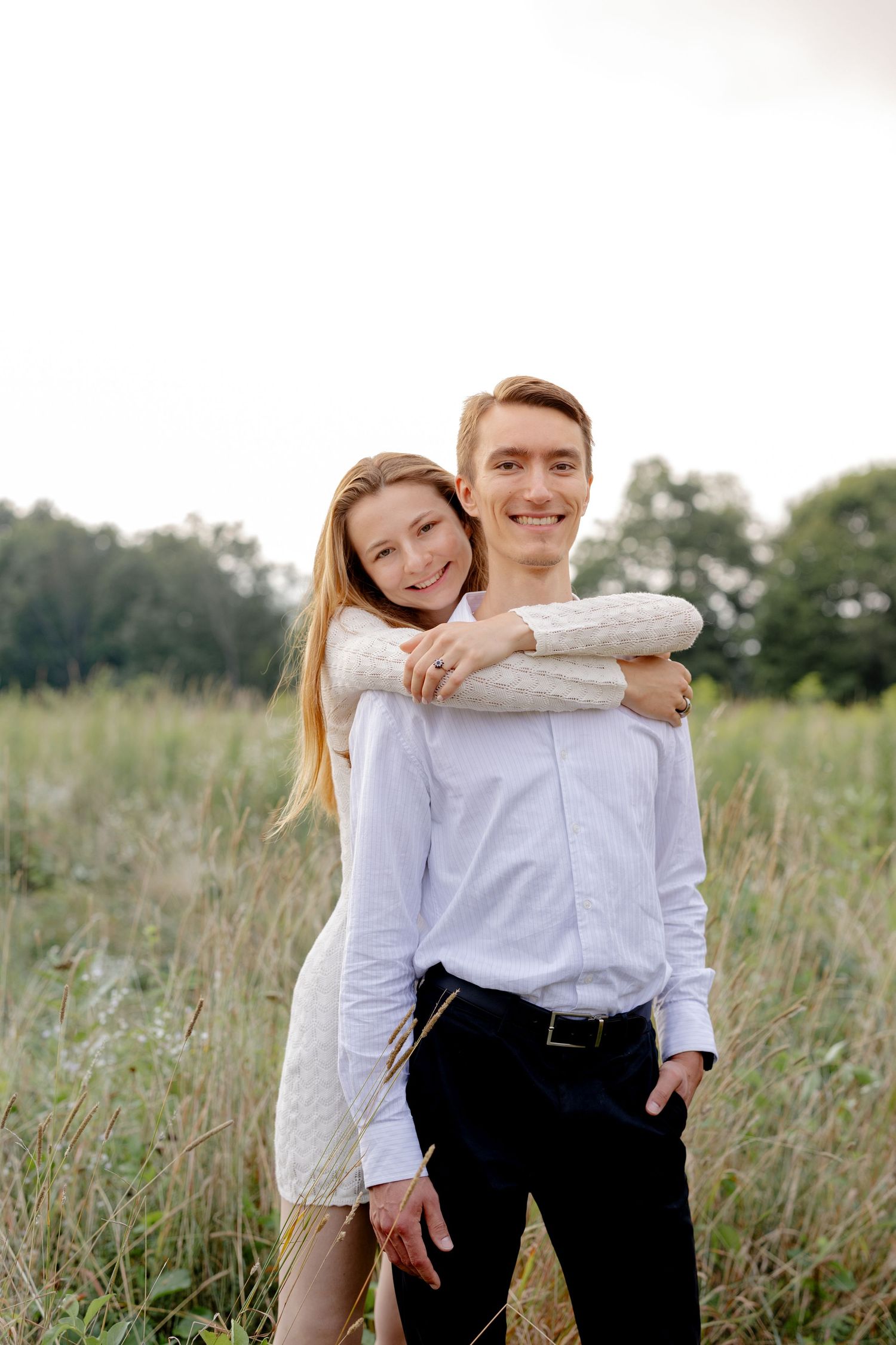 A couple poses playfully in a sunlit meadow wearing coordinated white and black outfits.
