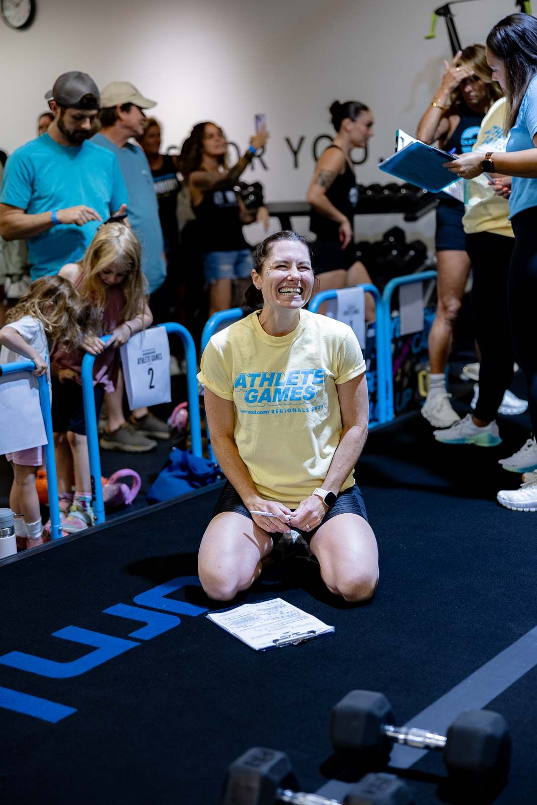 Collegiate women athletes sit on mats during a team gathering in a blue-floored gymnasium.