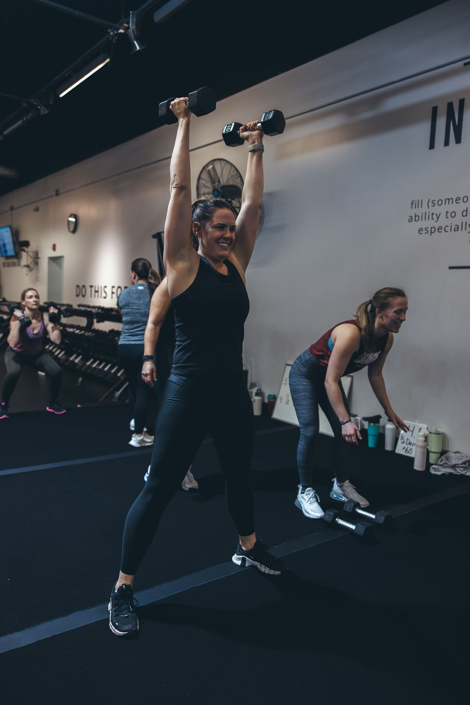 Fitness participants performing overhead dumbbell exercises during group training session.