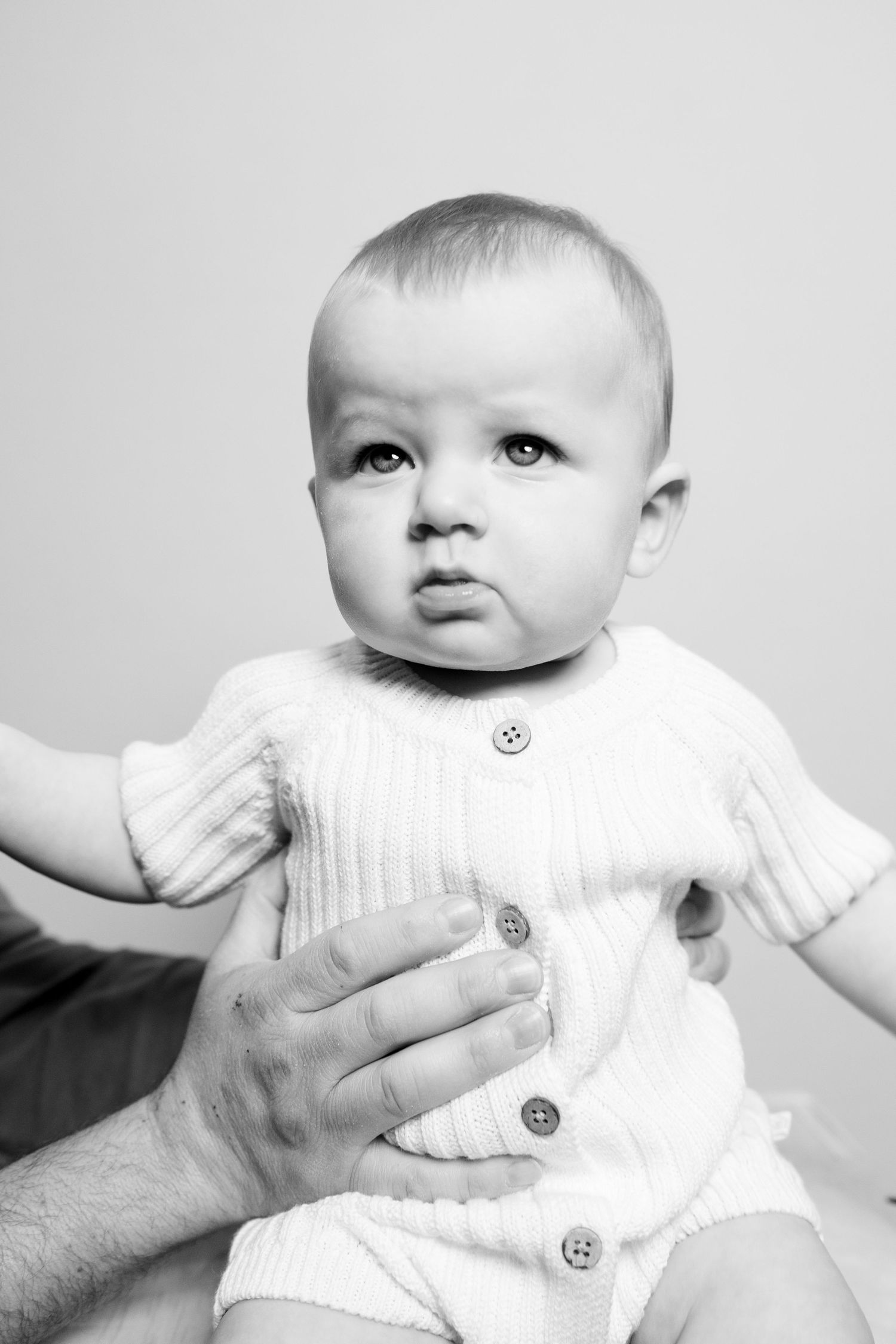 A series of four black and white photos showing a baby in a white outfit being held by adult hands.