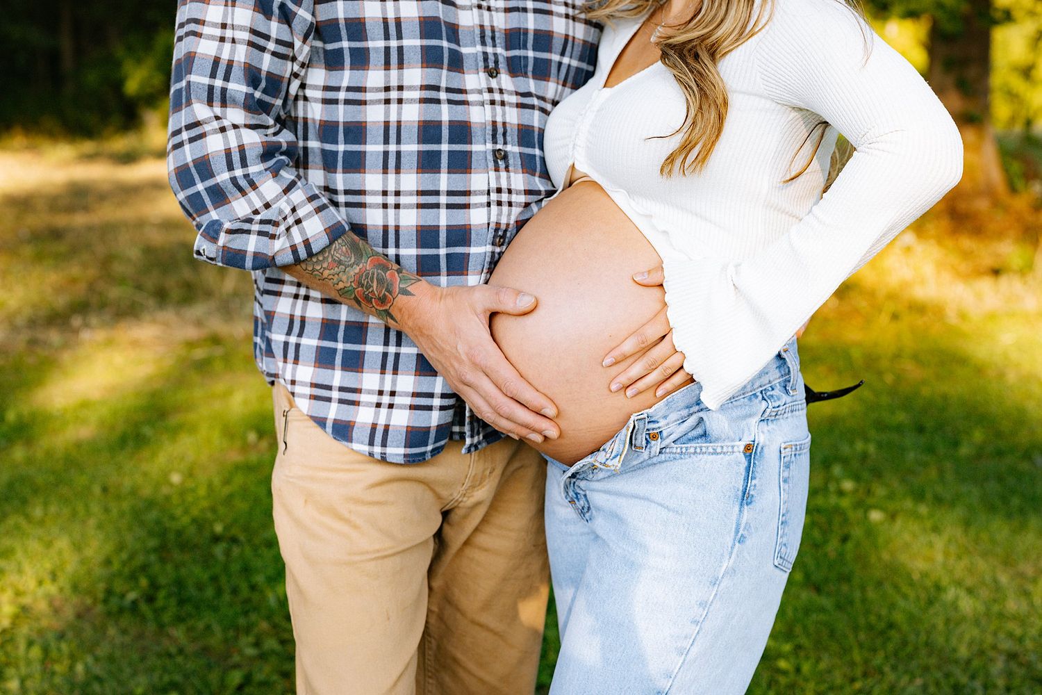 Cropped shot of couple's hands cradling pregnant belly in outdoor setting.