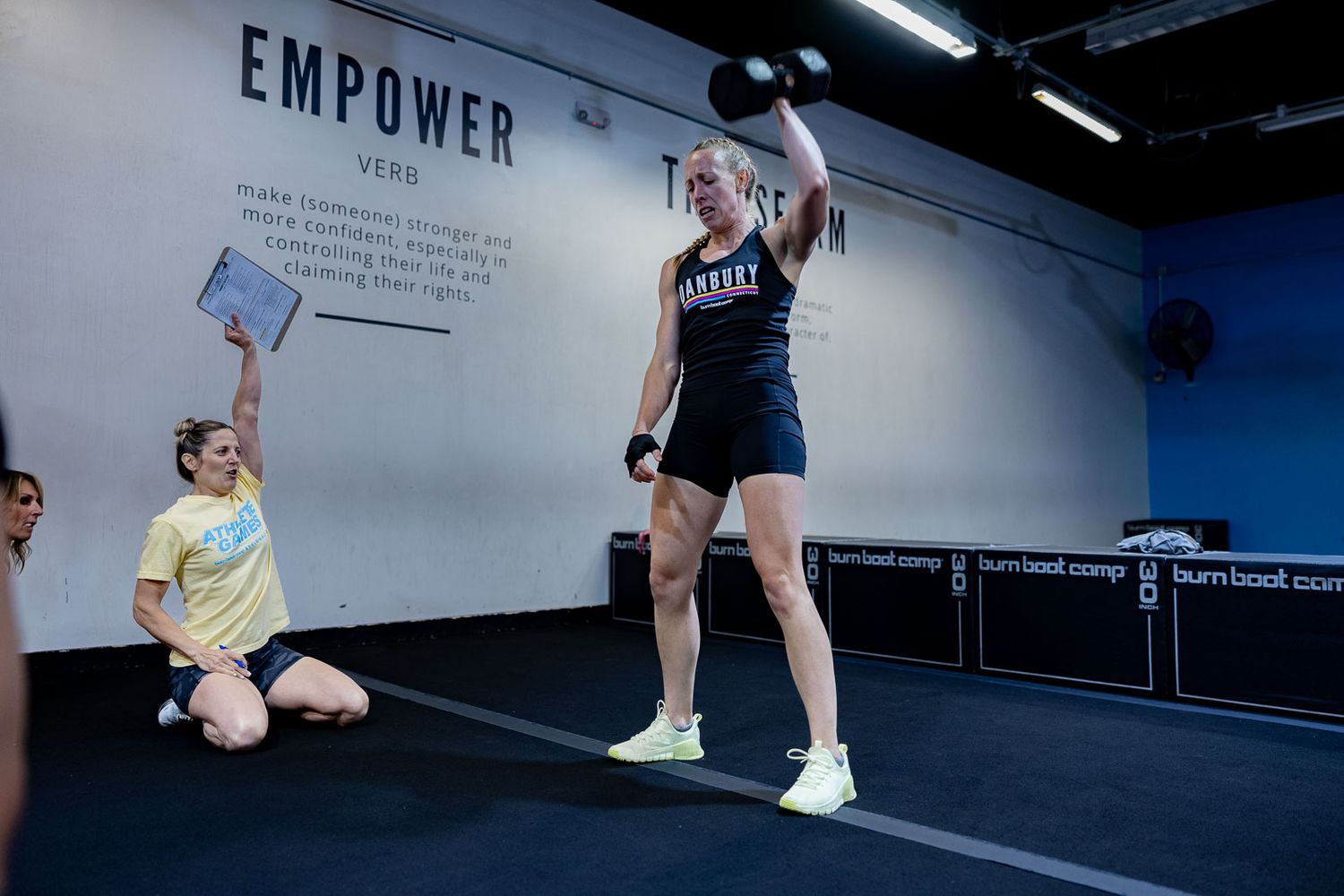 Athletes working out in a gym with an 'Empower' sign on the wall as one person performs an overhead exercise.