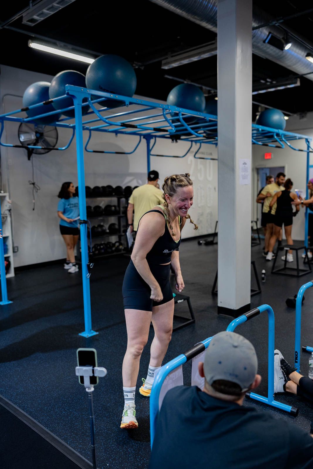 Athlete performs workout exercises at a gym facility with blue overhead equipment racks.
