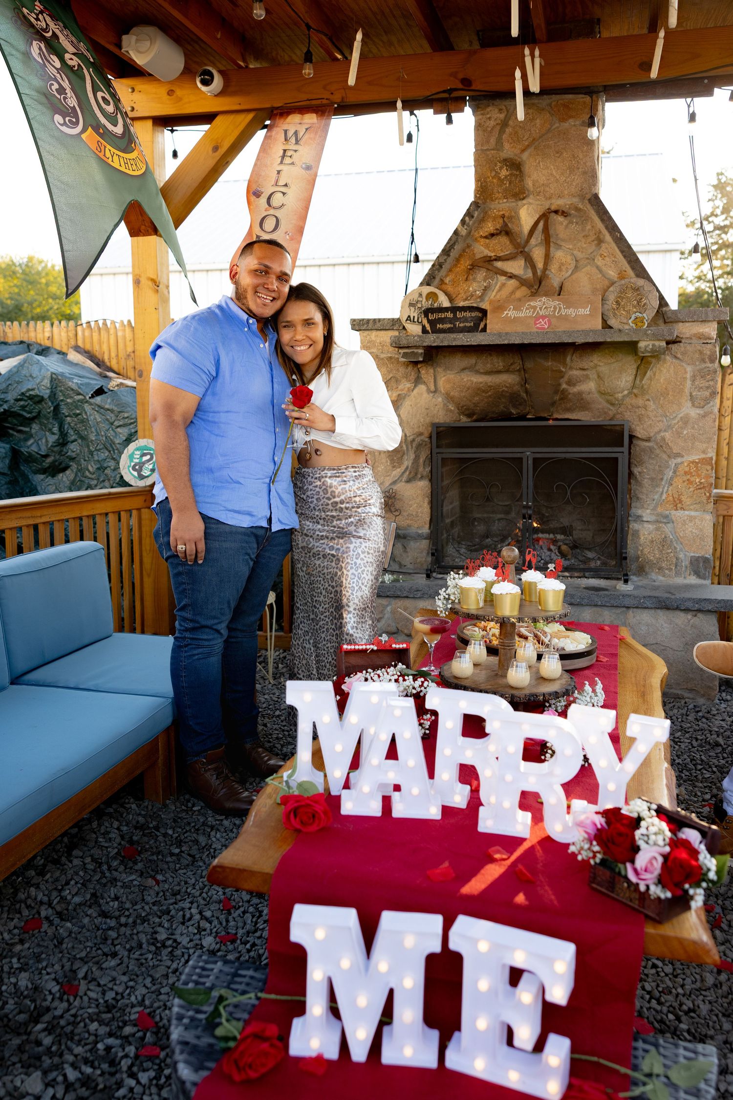 Rustic outdoor setting with large 'MARRY ME' letters decorated with red roses and white decor.