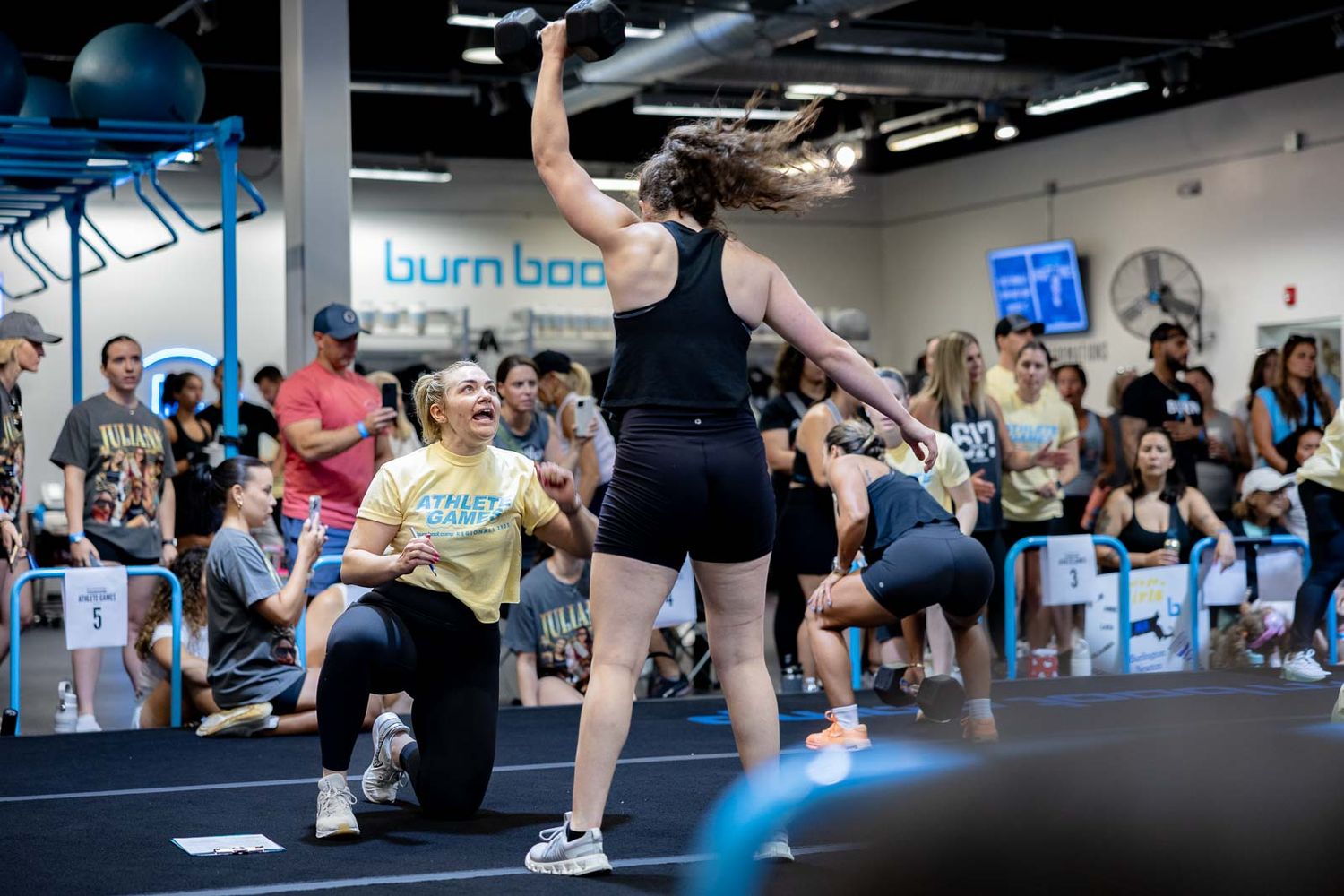 Athletes in a gym participate in a high-energy fitness class with spectators watching from the sidelines.