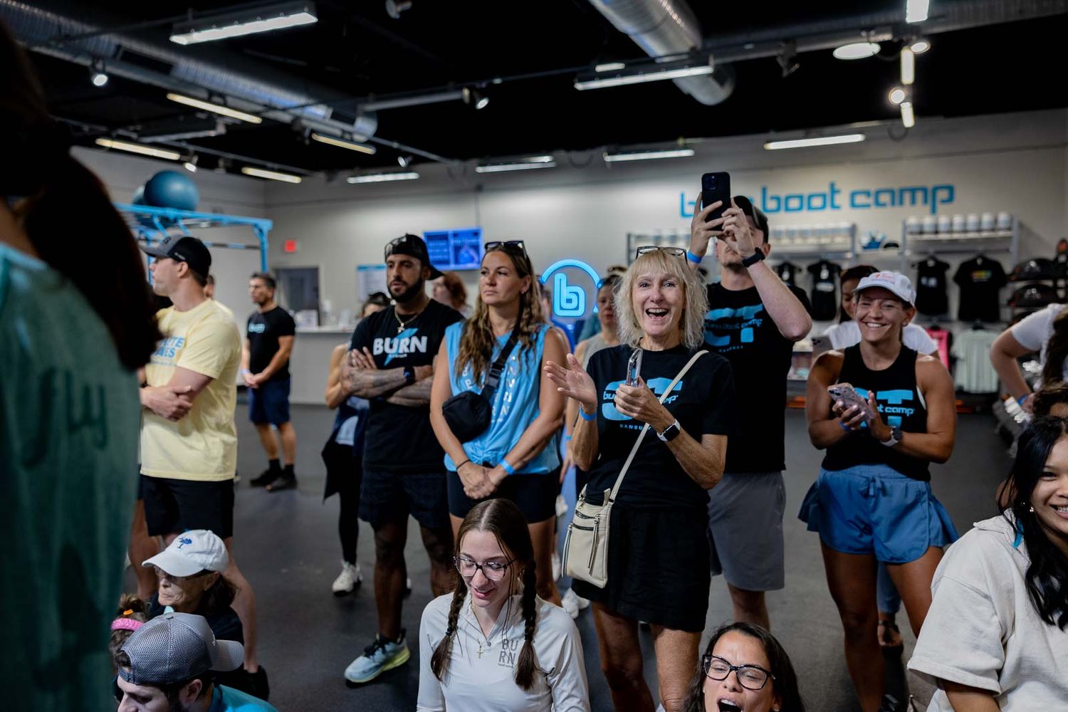 A group of people wearing black t-shirts gather in an indoor venue looking upward with excited expressions.