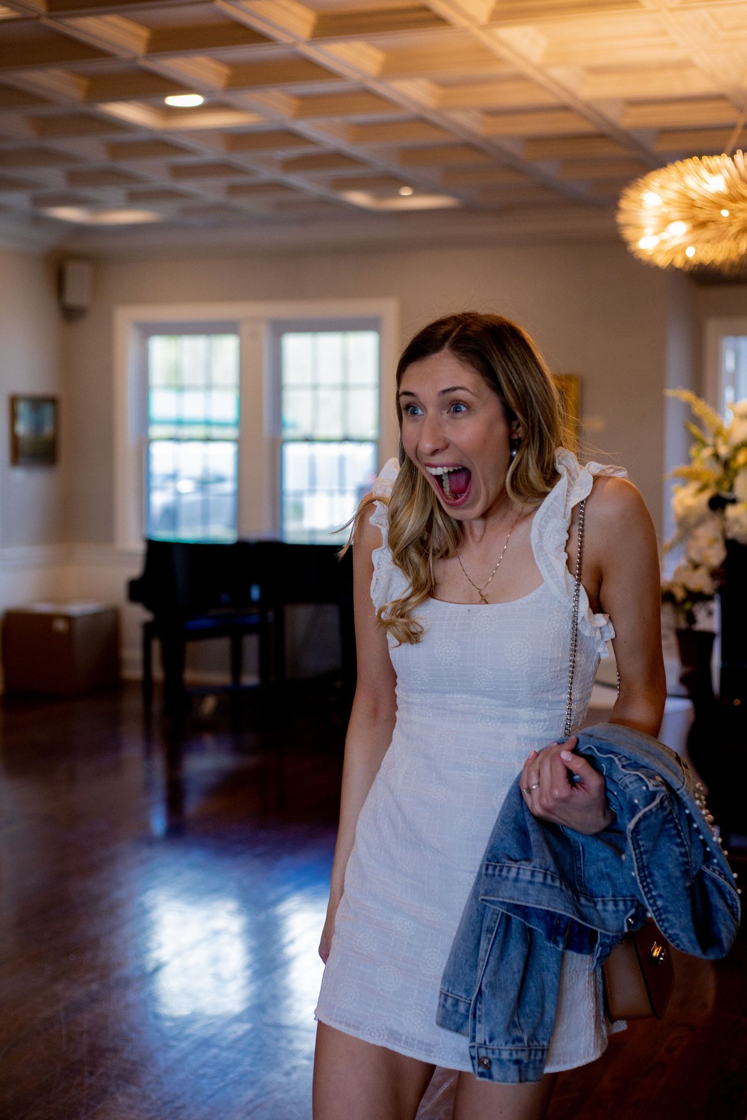A person in a white dress shows excitement in an indoor venue with wooden floors.