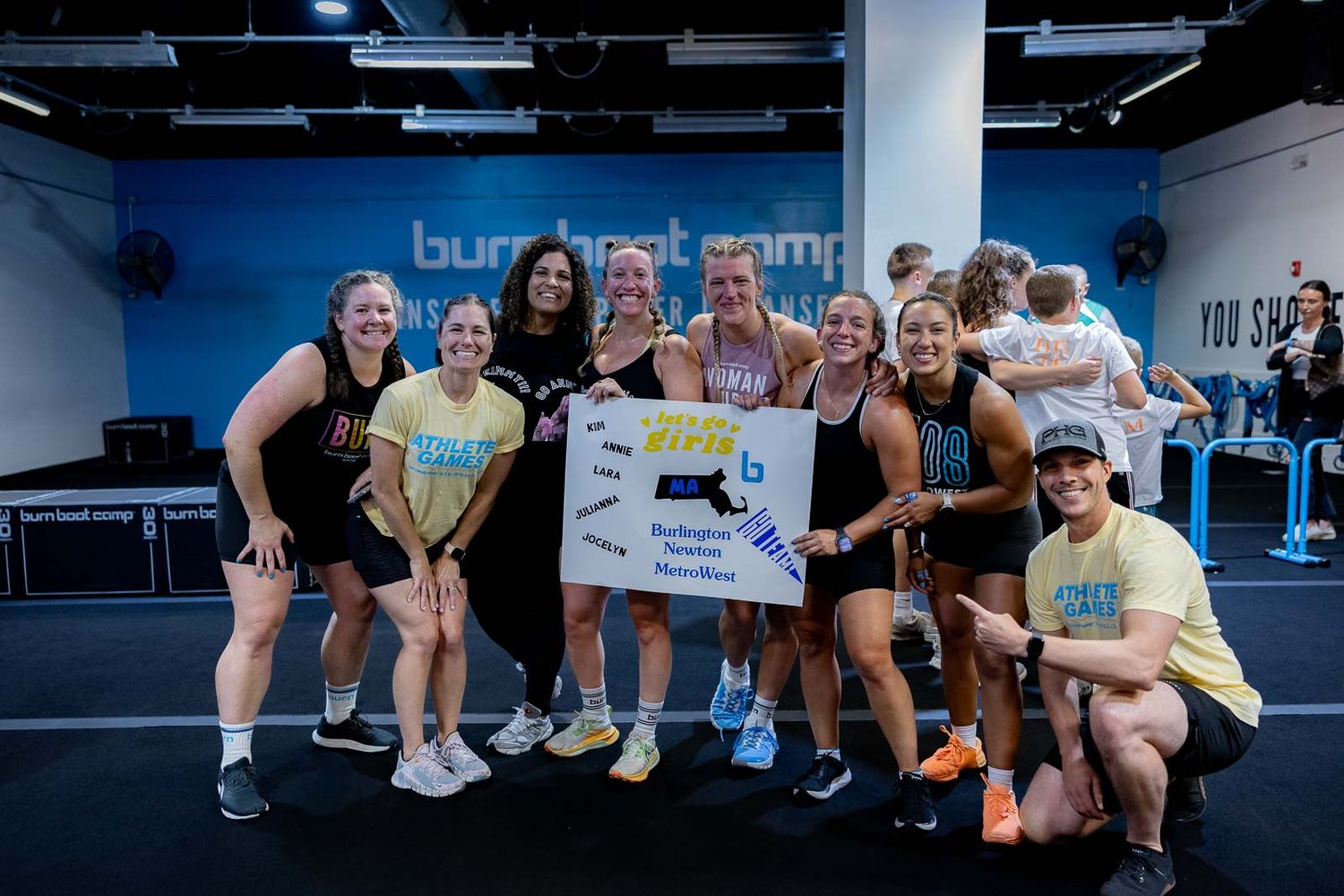 A group gathers for a celebratory photo in a blue-walled fitness studio space.