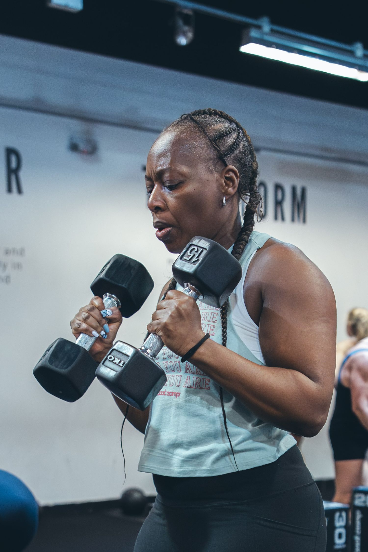 Athletic woman performing dumbbell exercises in a fitness studio with motivational wall text.