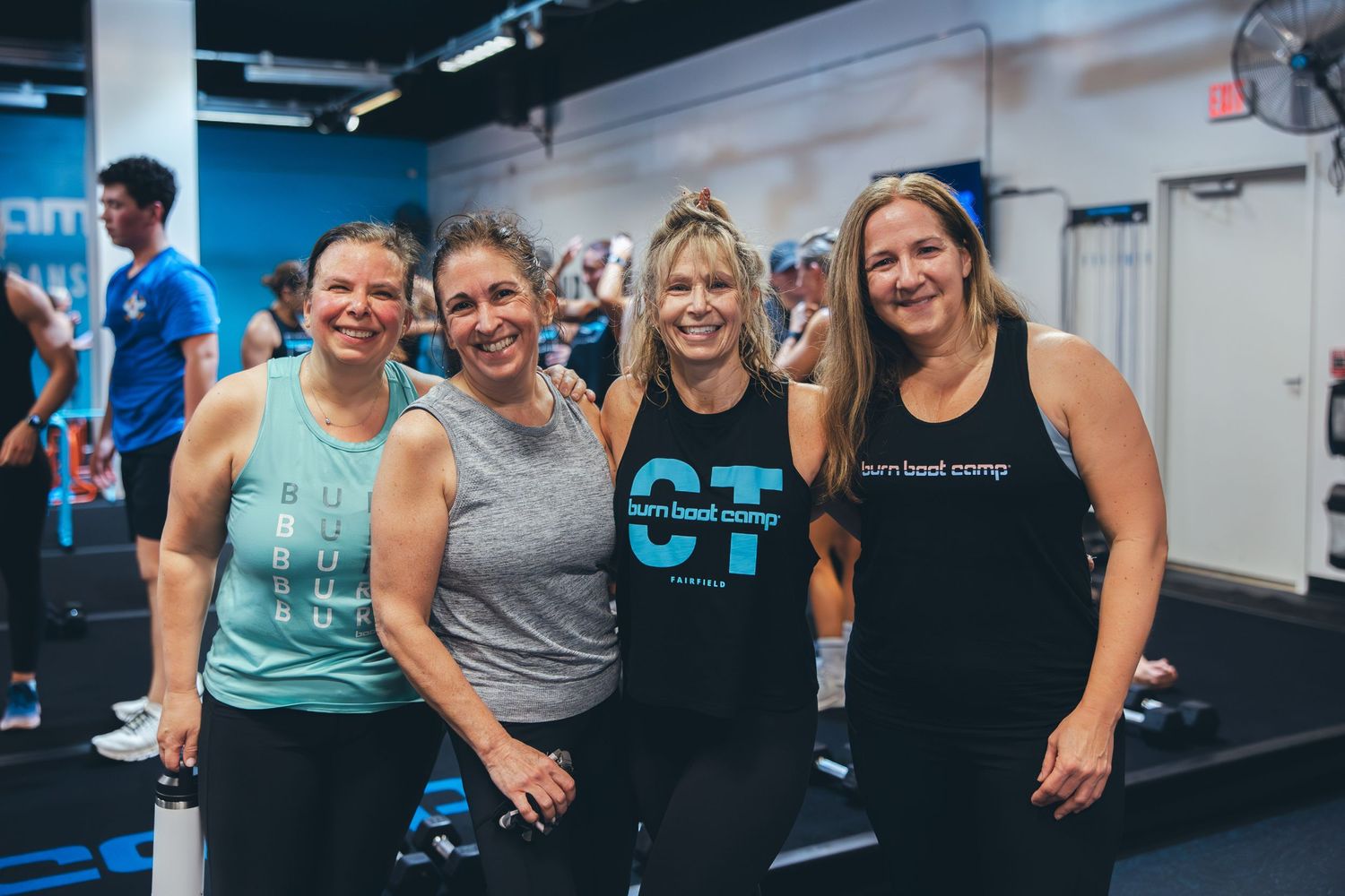 Four fitness trainers smiling and posing together at Burn Boot Camp gym.