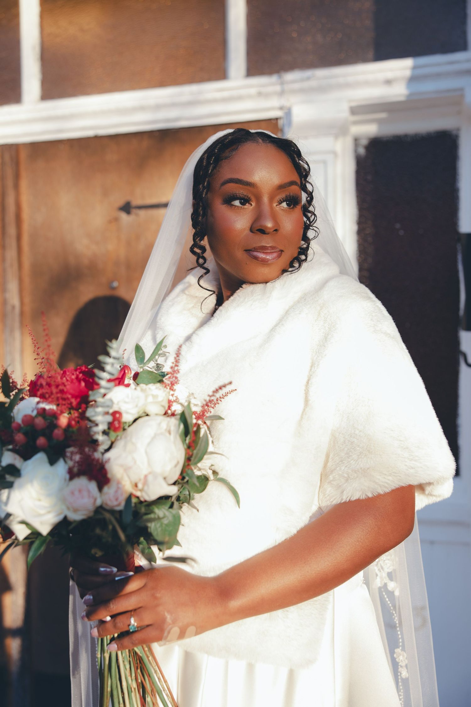 Elegant bride in a white winter wedding dress with fur wrap holds a vibrant red and white bouquet.