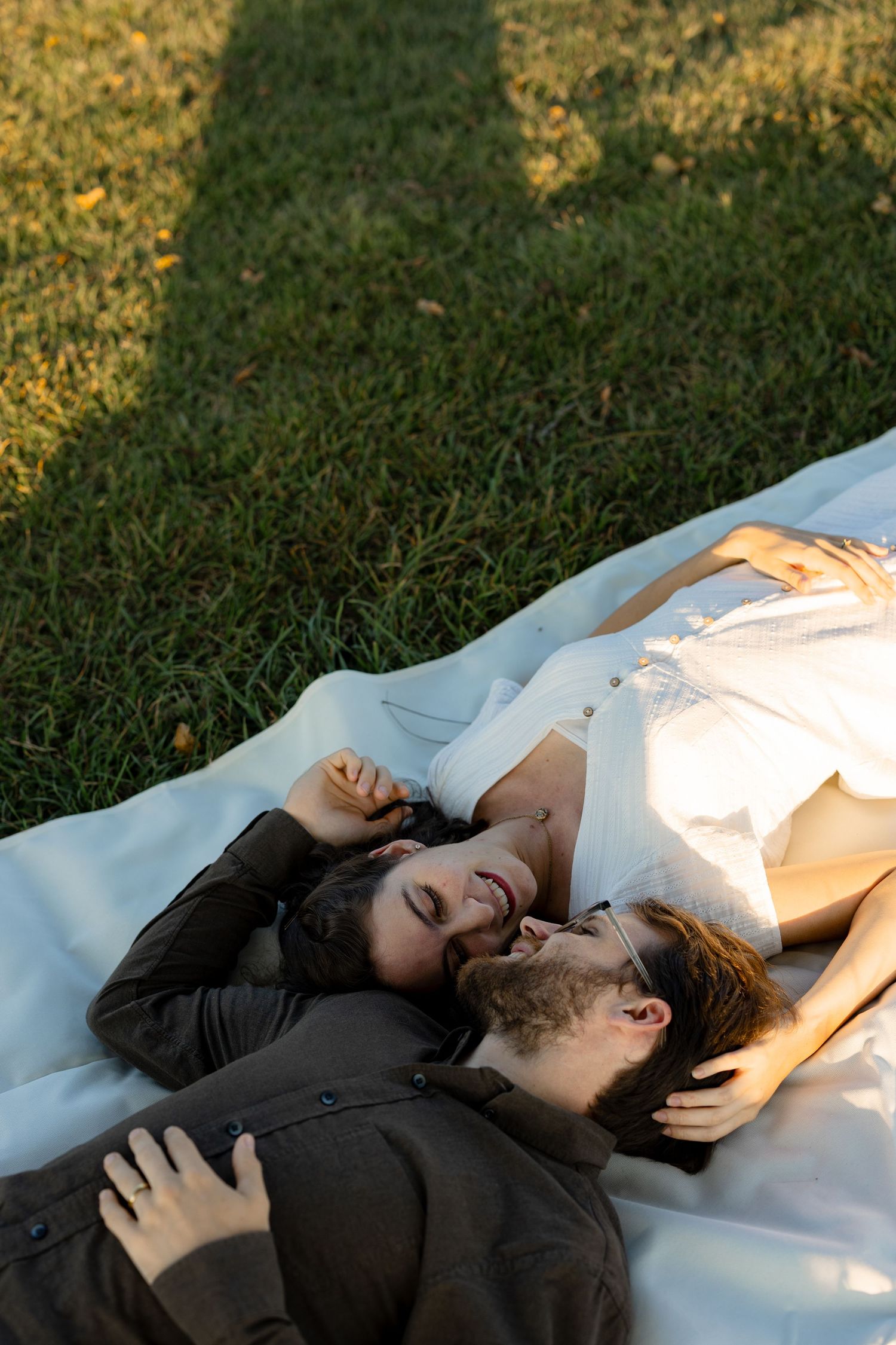 Two people lying on a white blanket in the grass during golden hour sunlight.