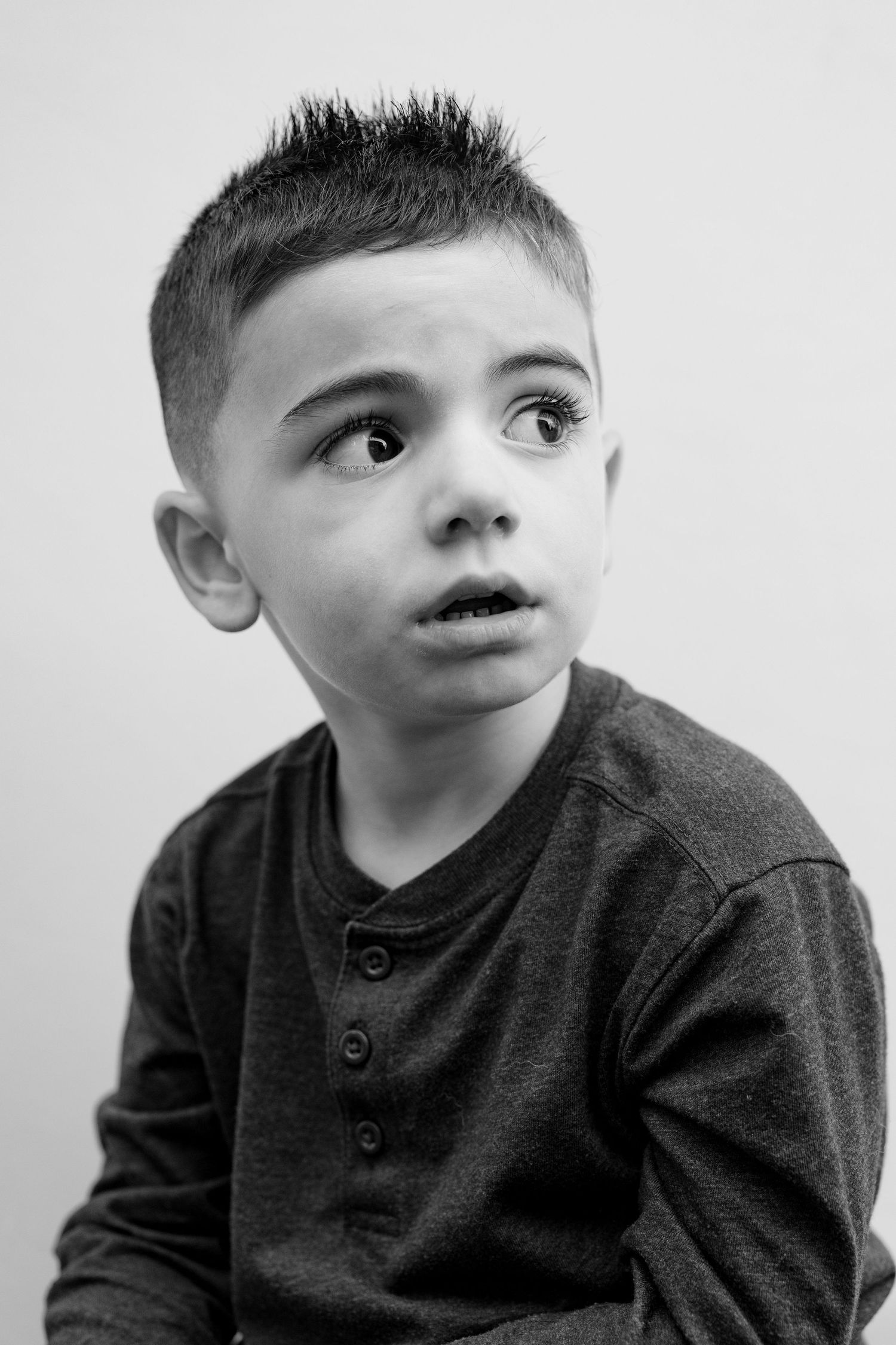 A black and white portrait series showing different angles of a young child wearing a dark henley shirt.